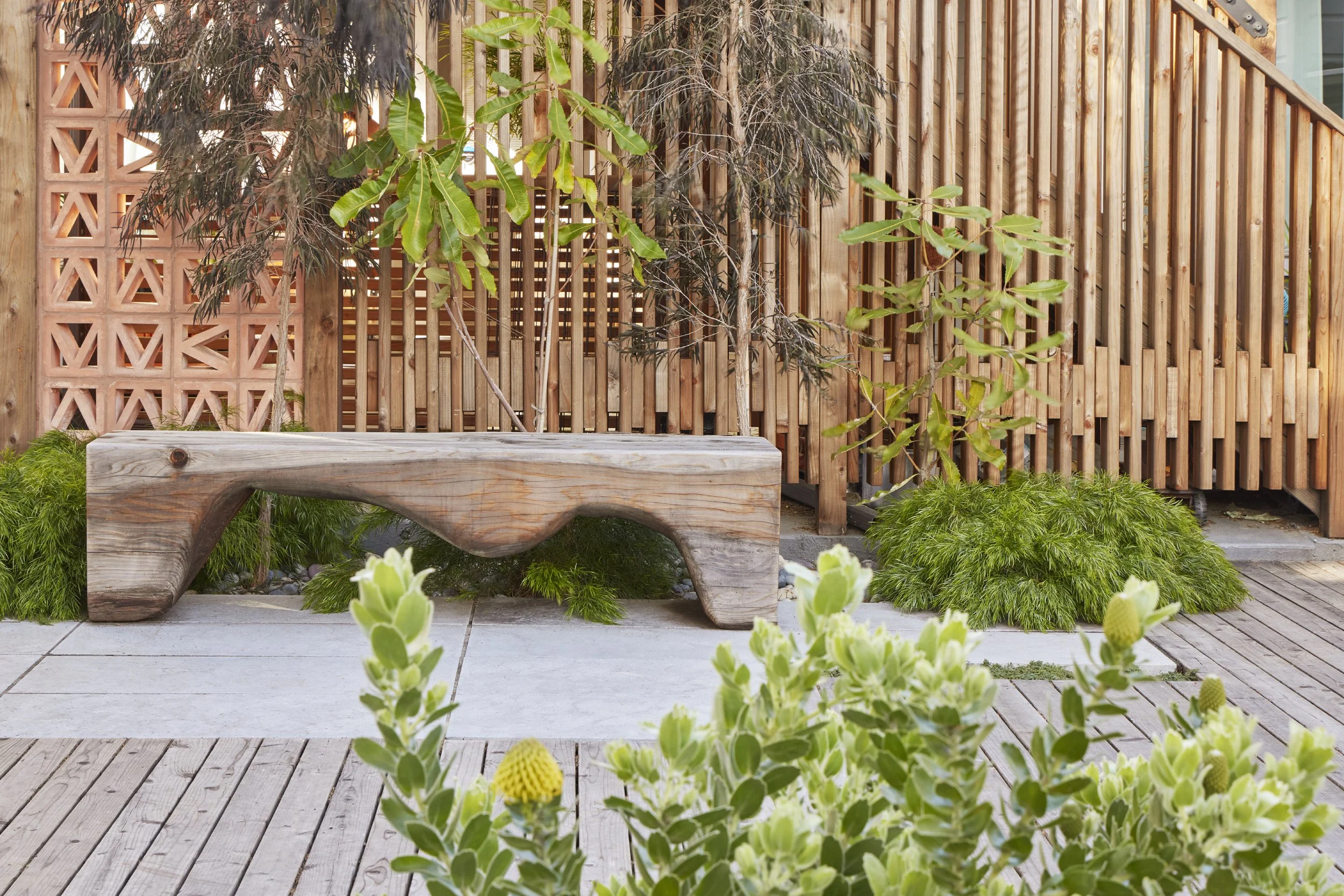 A modern outdoor garden space with a wooden bench, green plants, and a wooden lattice fence.