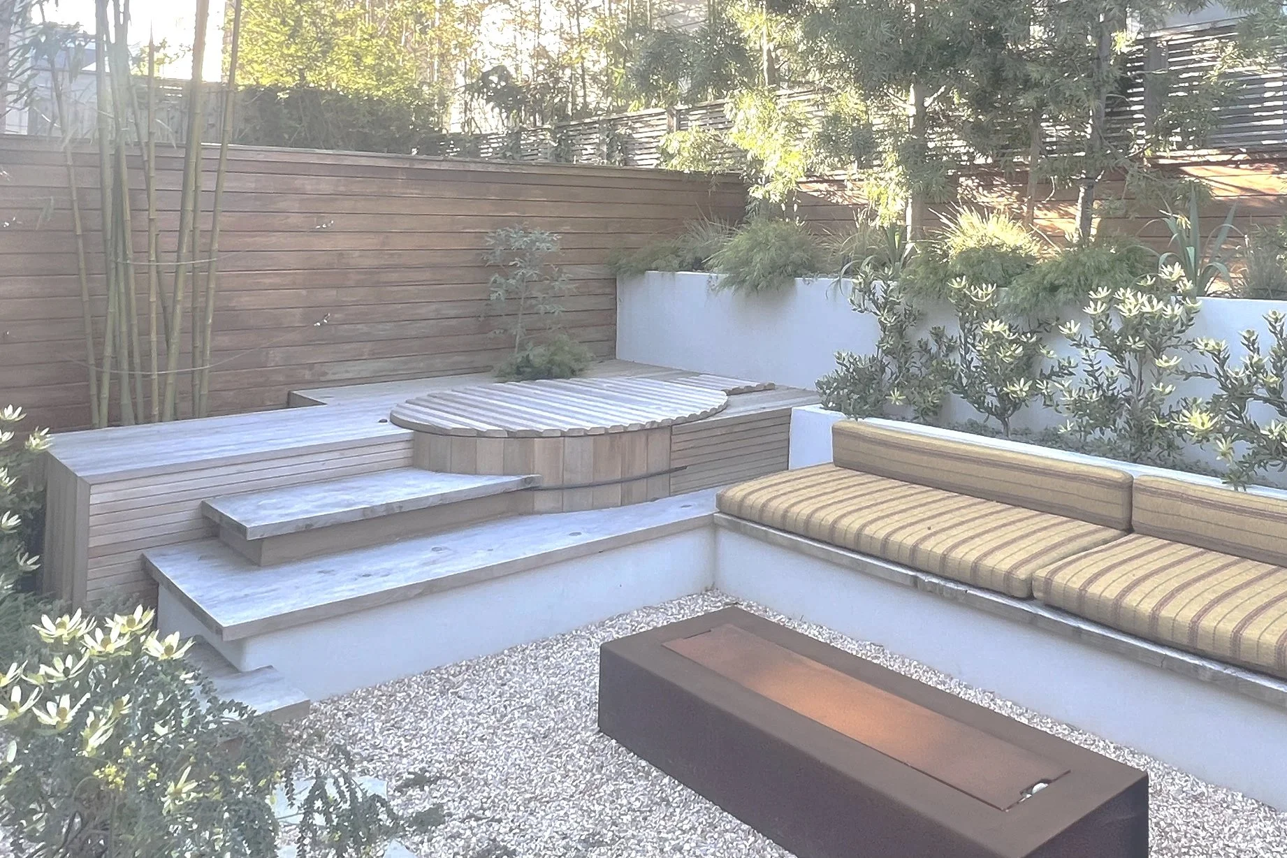 Modern outdoor seating area with built-in benches, a fire pit, and lush plants.