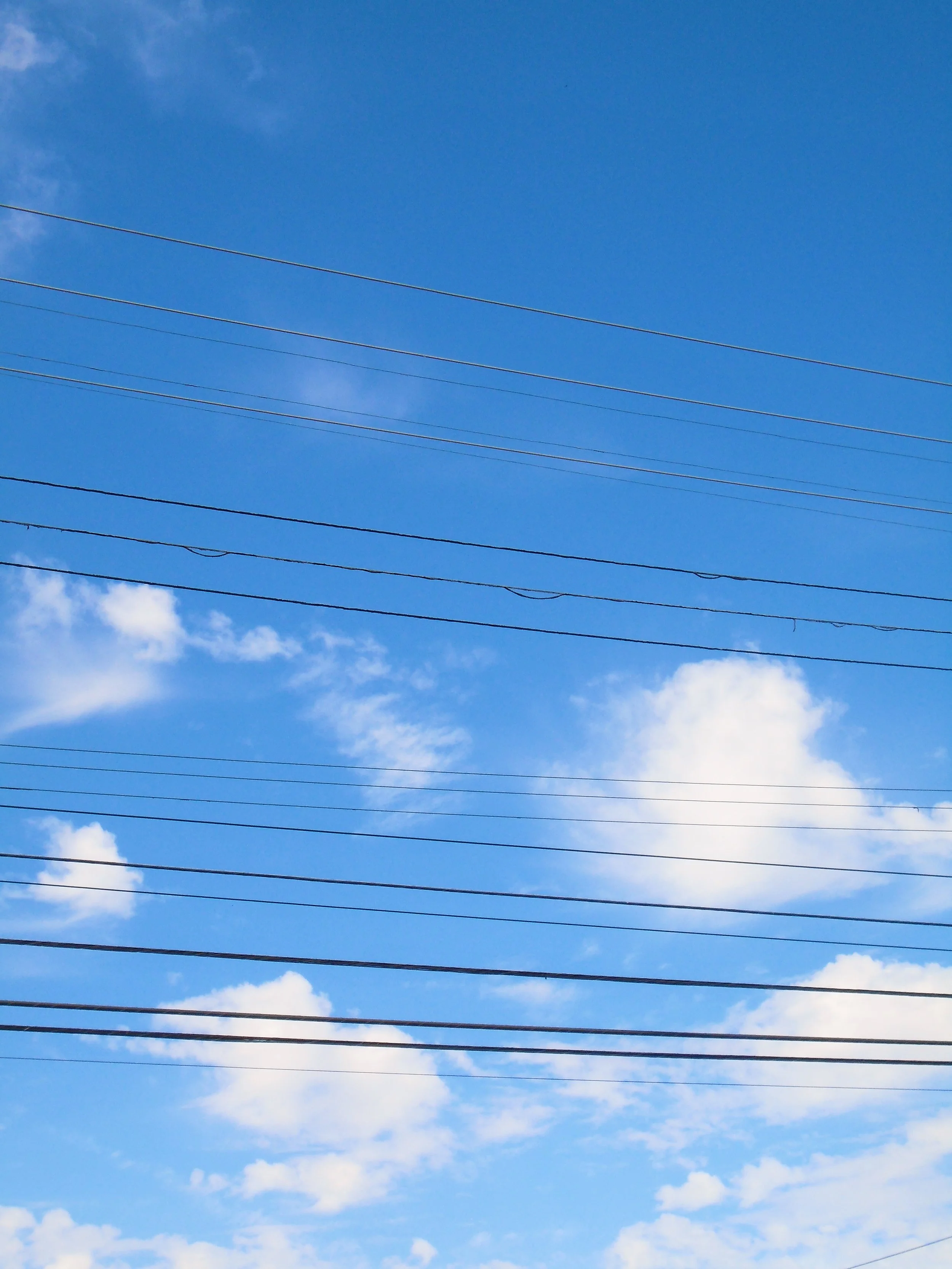 Blue sky with scattered clouds and multiple overhead power lines.