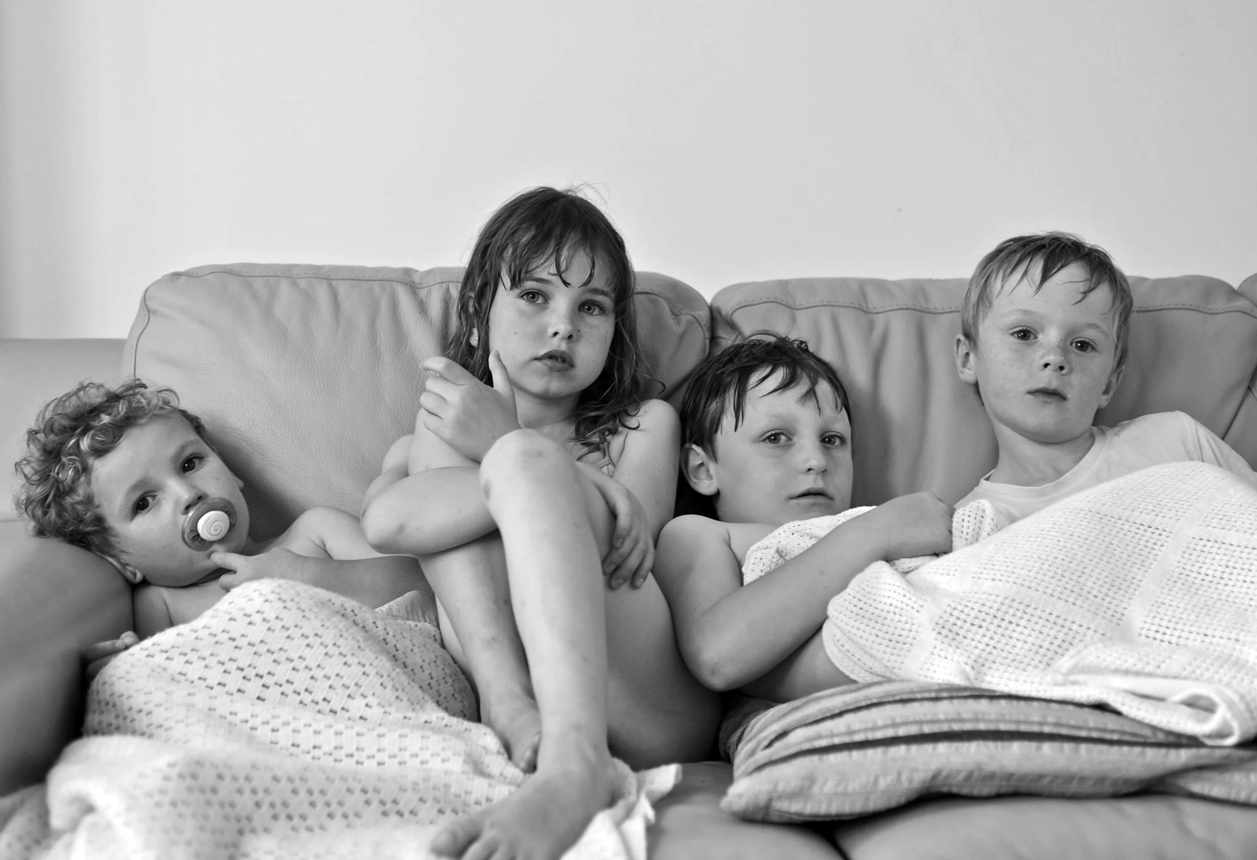 Four children sitting on a couch, with one baby lying down, in black and white.