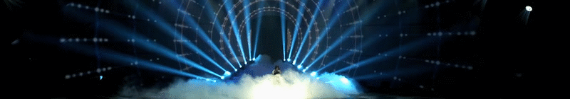 A performer on a stage with blue laser lights and fog effects.