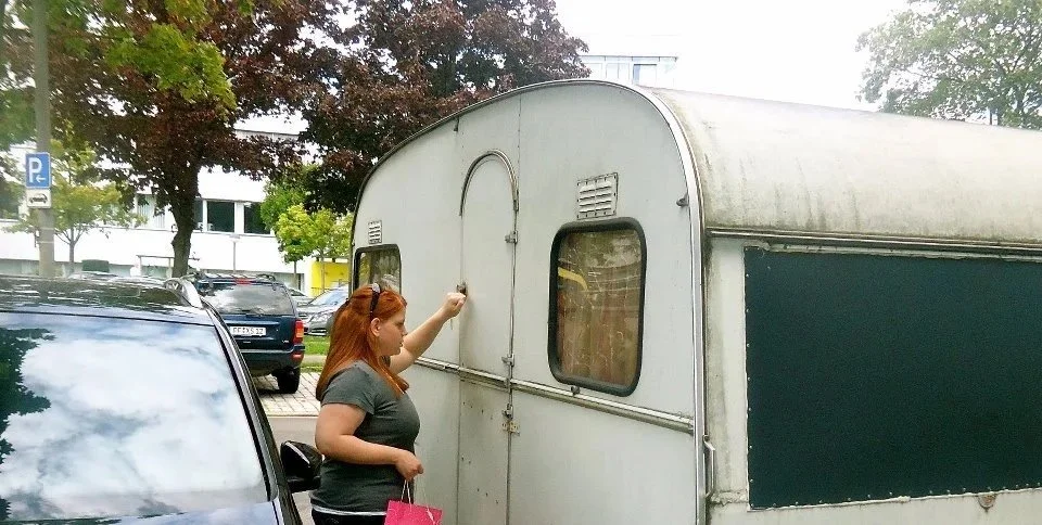 Eine rothaarige Frau steht neben einem Auto und einem Wohnwagen, während sie den Wohnwagen abschließt oder abschließt.