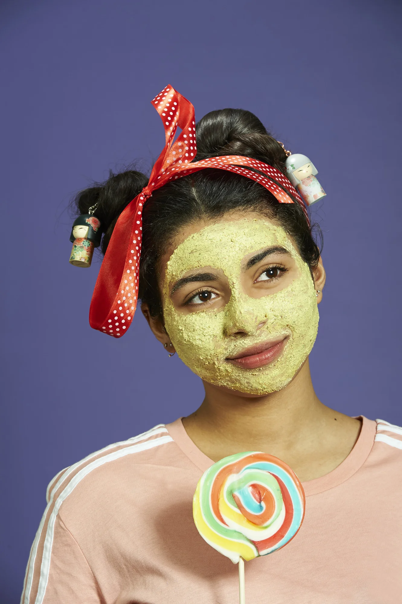 Photo of a teenage girl wearing a face pack, holding a large candy lolly.
