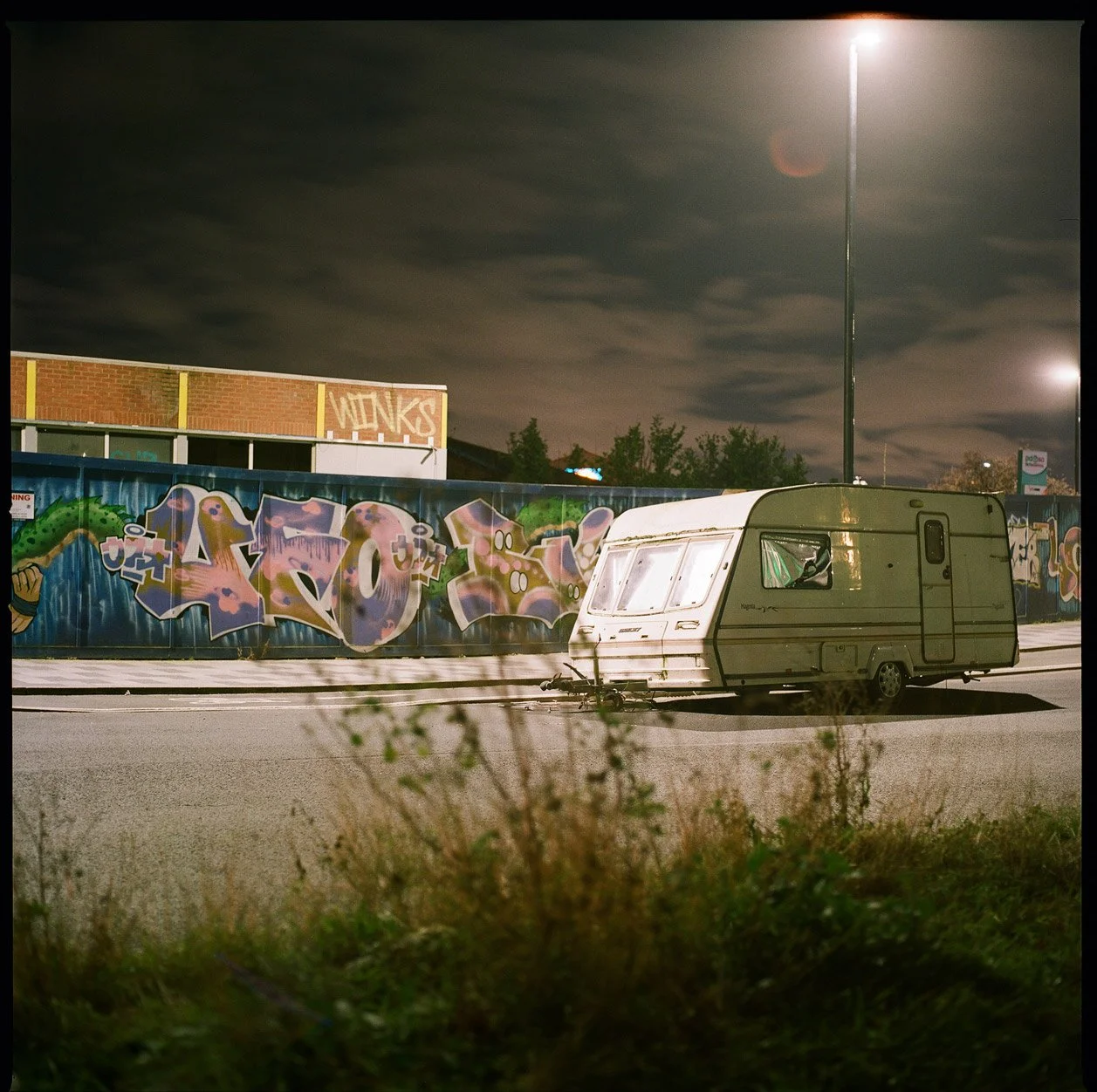Abandoned caravan - urban setting with graffitied hoarding -night light  
