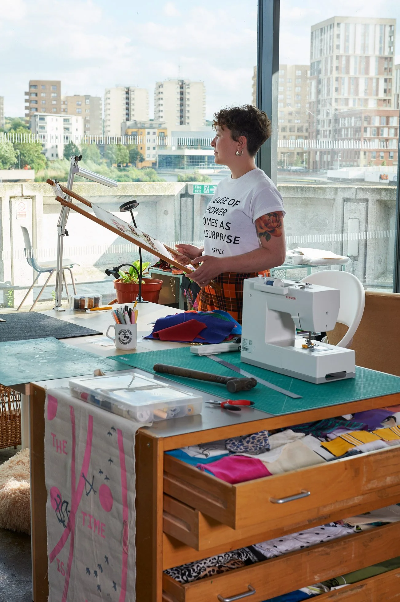 female artist in studio setting. She looks out of the window. 