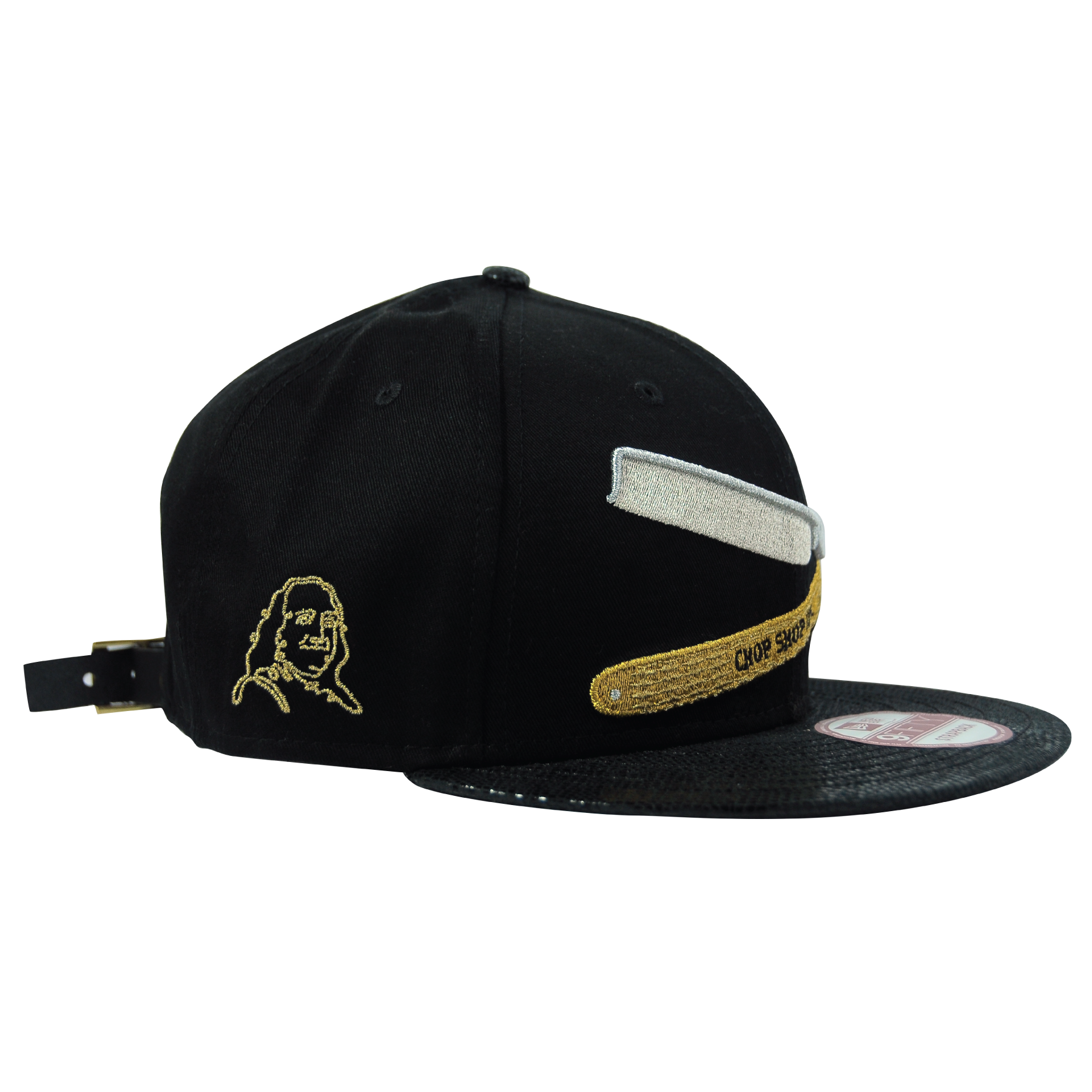 Black baseball cap with embroidered image of a person and patches, including a white rectangular patch, a gold belt patch with text, and a side embroidered face, facing left, on the left side of the cap.