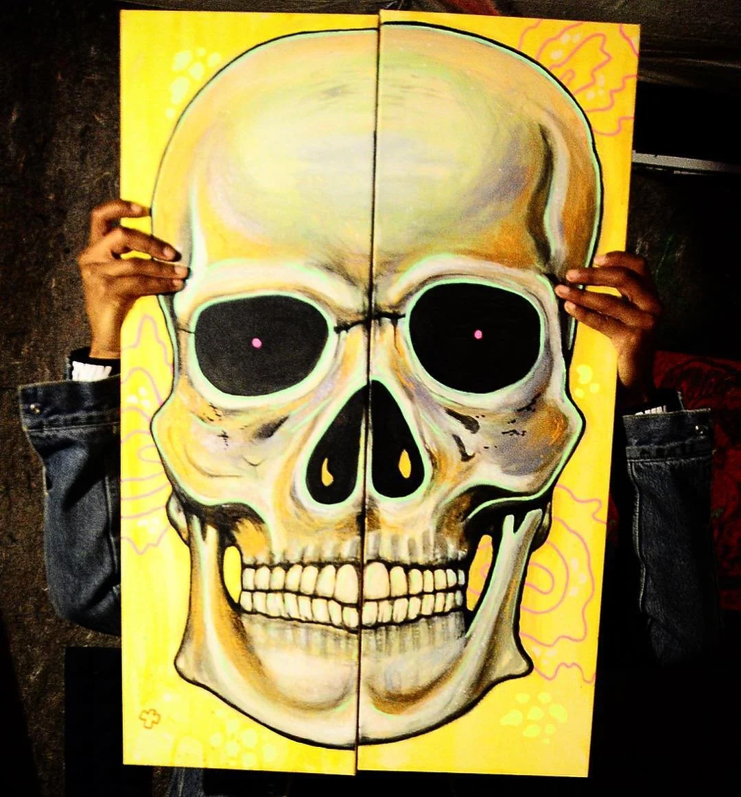 A person holding a painting of a skull with a yellow background.