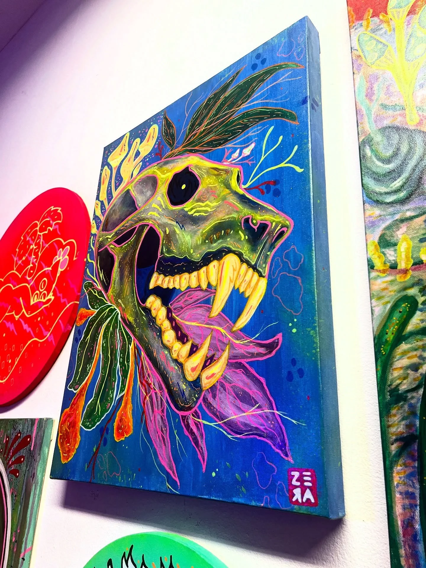 A colorful painting of a dinosaur skull with feathers, leaves, and abstract patterns on a blue background.