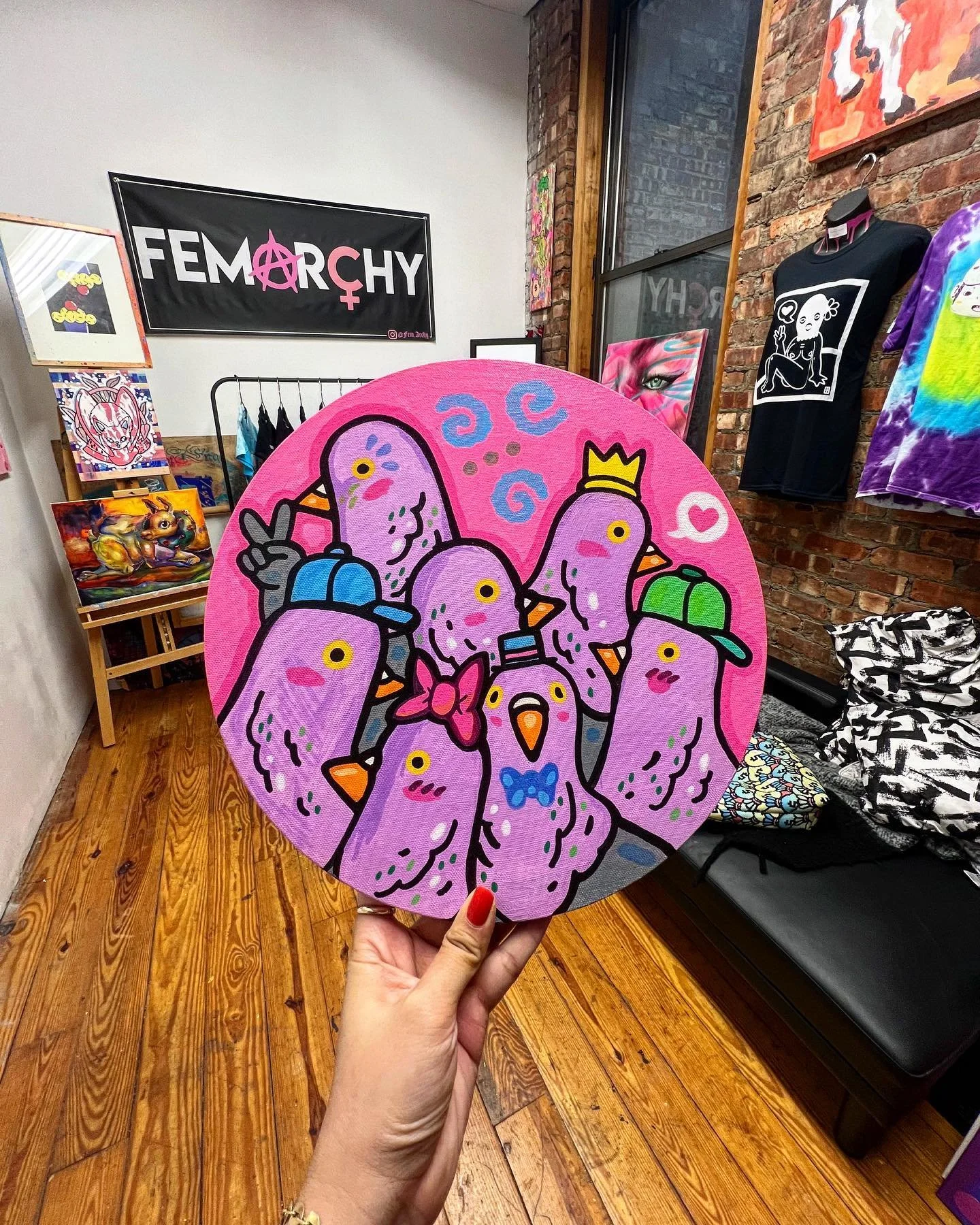 A brightly colored round artwork featuring cartoon-style drawn purple birds with orange beaks, some wearing caps, bows, and a crown. The background is pink with blue swirls and a white heart.