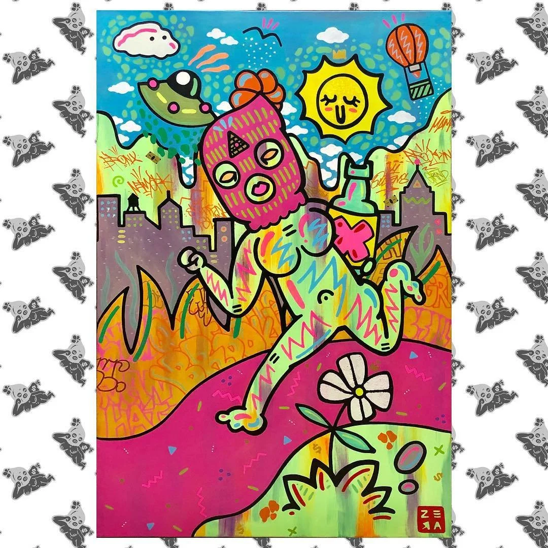 Colorful street art depicting a surreal scene with a figure wearing a pink mask with yellow eyes, sitting on a pink hill with a flower and a mushroom. The background includes city buildings, a smiling sun, clouds, a rainbow, a hot air balloon, and a 