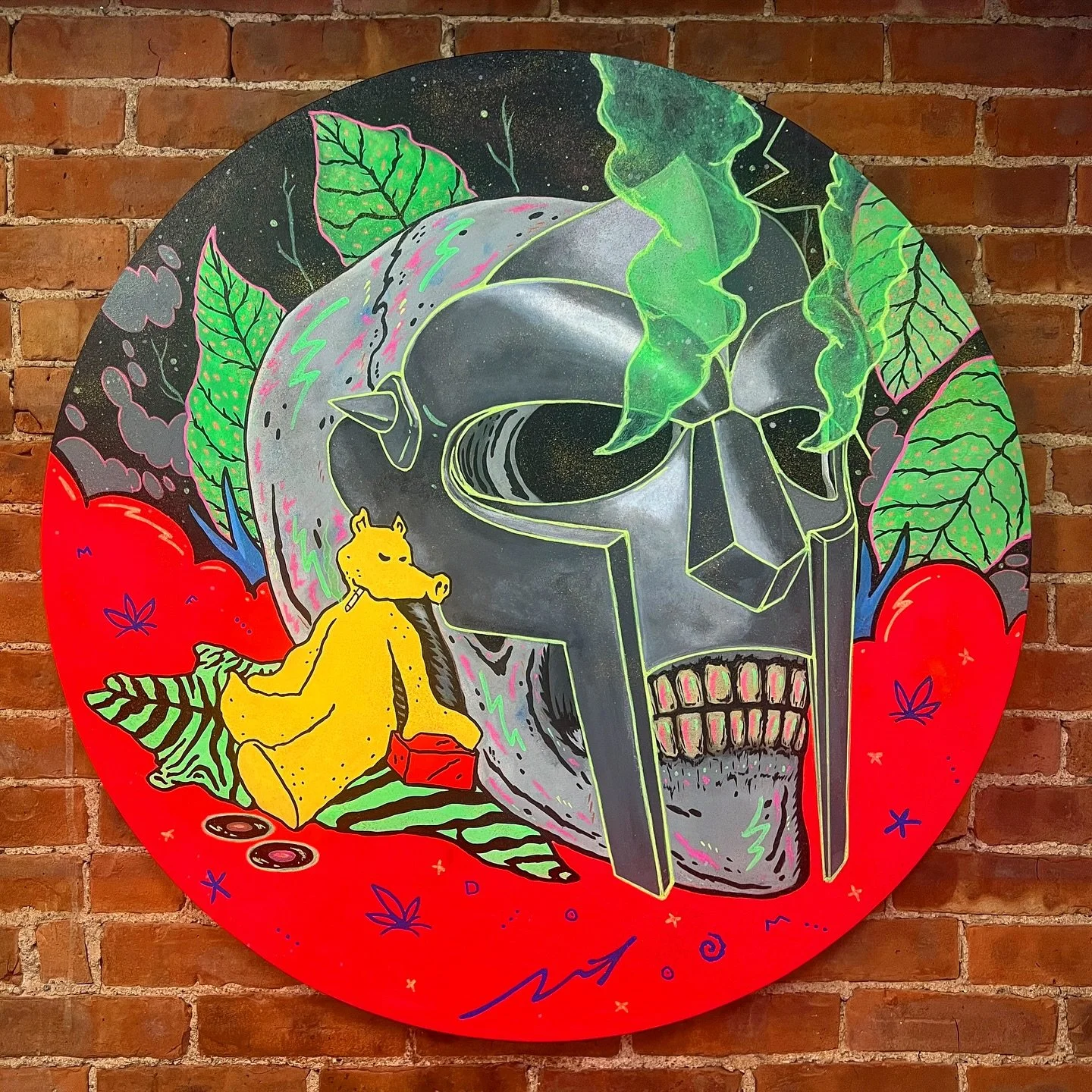 A colorful artistic painting featuring a large skull with a unicorn horn, surrounded by green leaves, red strawberries, and a yellow bear sitting on the ground holding a red box, all set against a brick wall background.