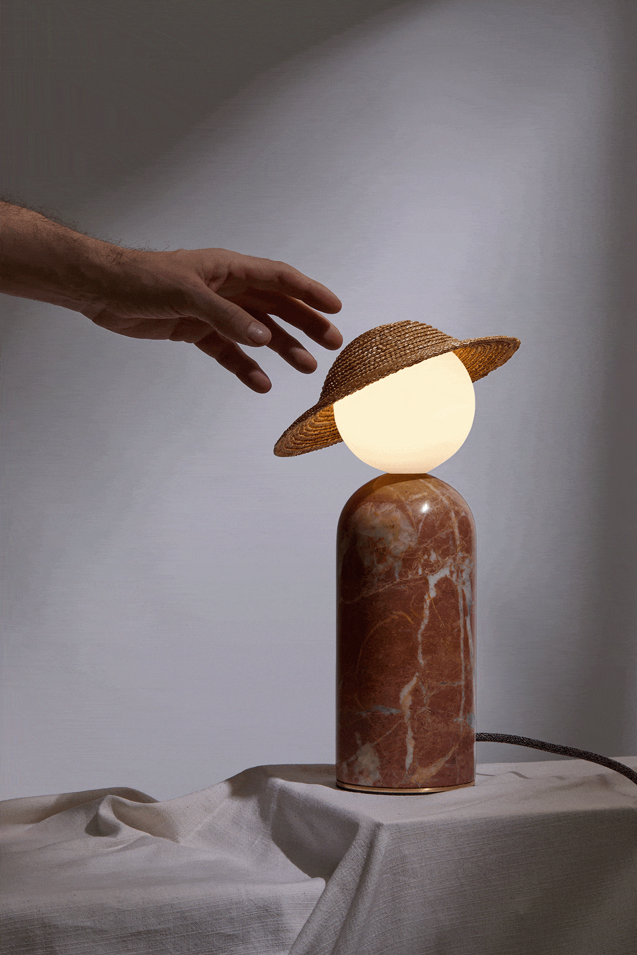  Each lamp’s body is made of marble, its head an opaque glass sphere,and its lampshade a handmade straw hat. The hat rests lightly on the glass sphere and can move freely in any direction, creating different lighting conditions and transforming the m
