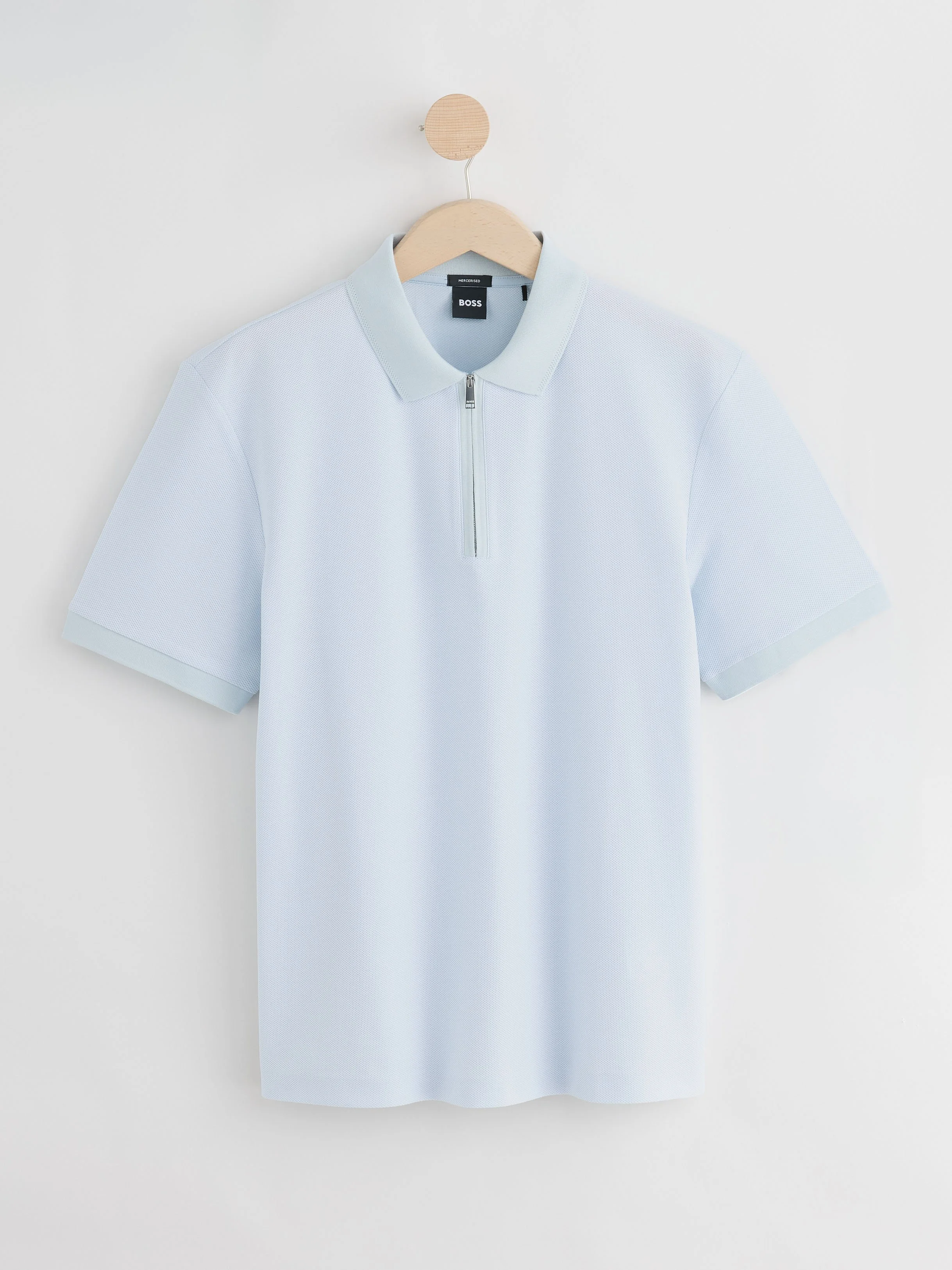 Light blue short-sleeve polo shirt with a zippered collar hanging on a wooden hanger against a white background.