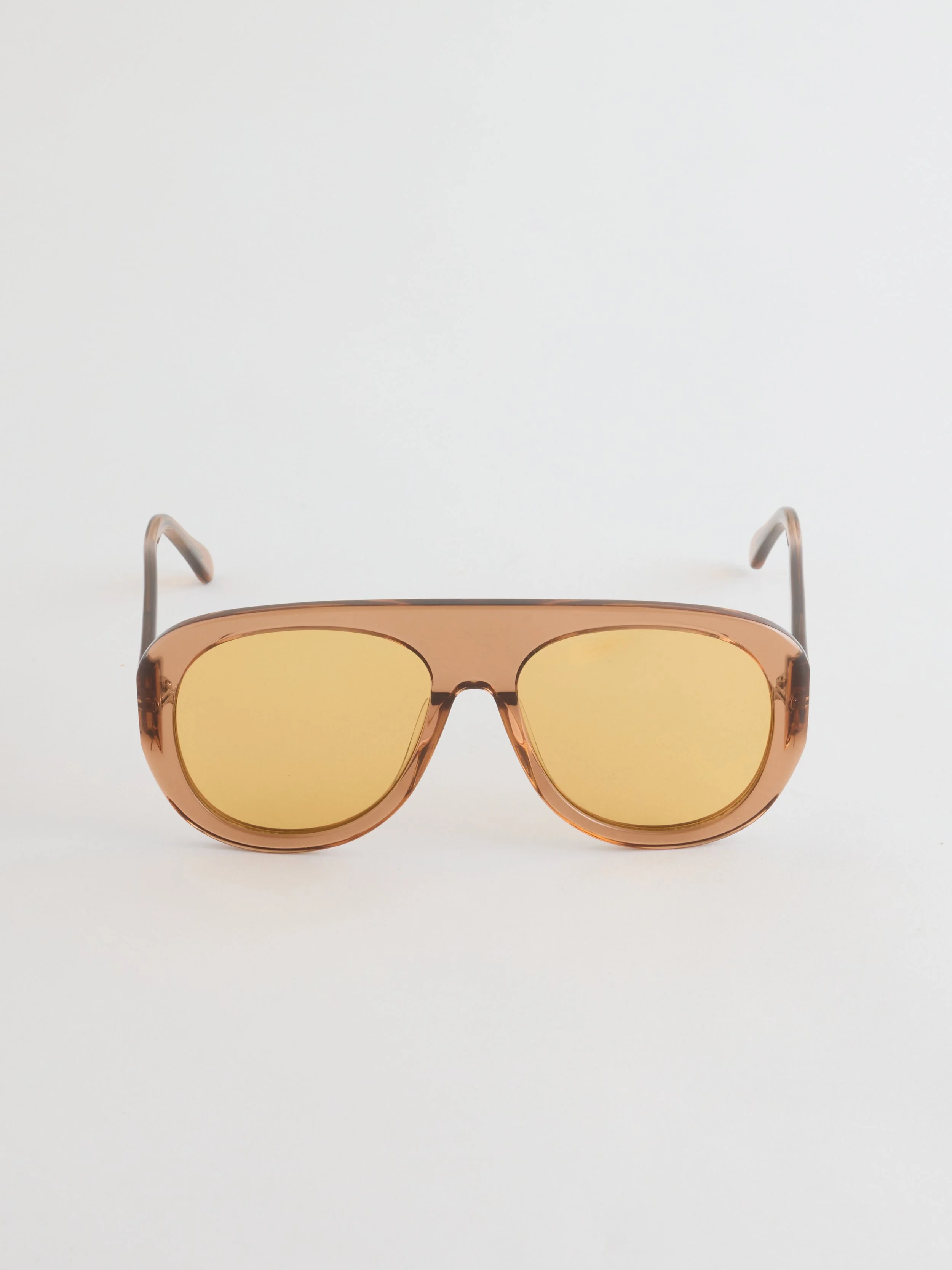 Fashion sunglasses with a transparent rose gold frame and yellow tinted lenses on a plain white surface.