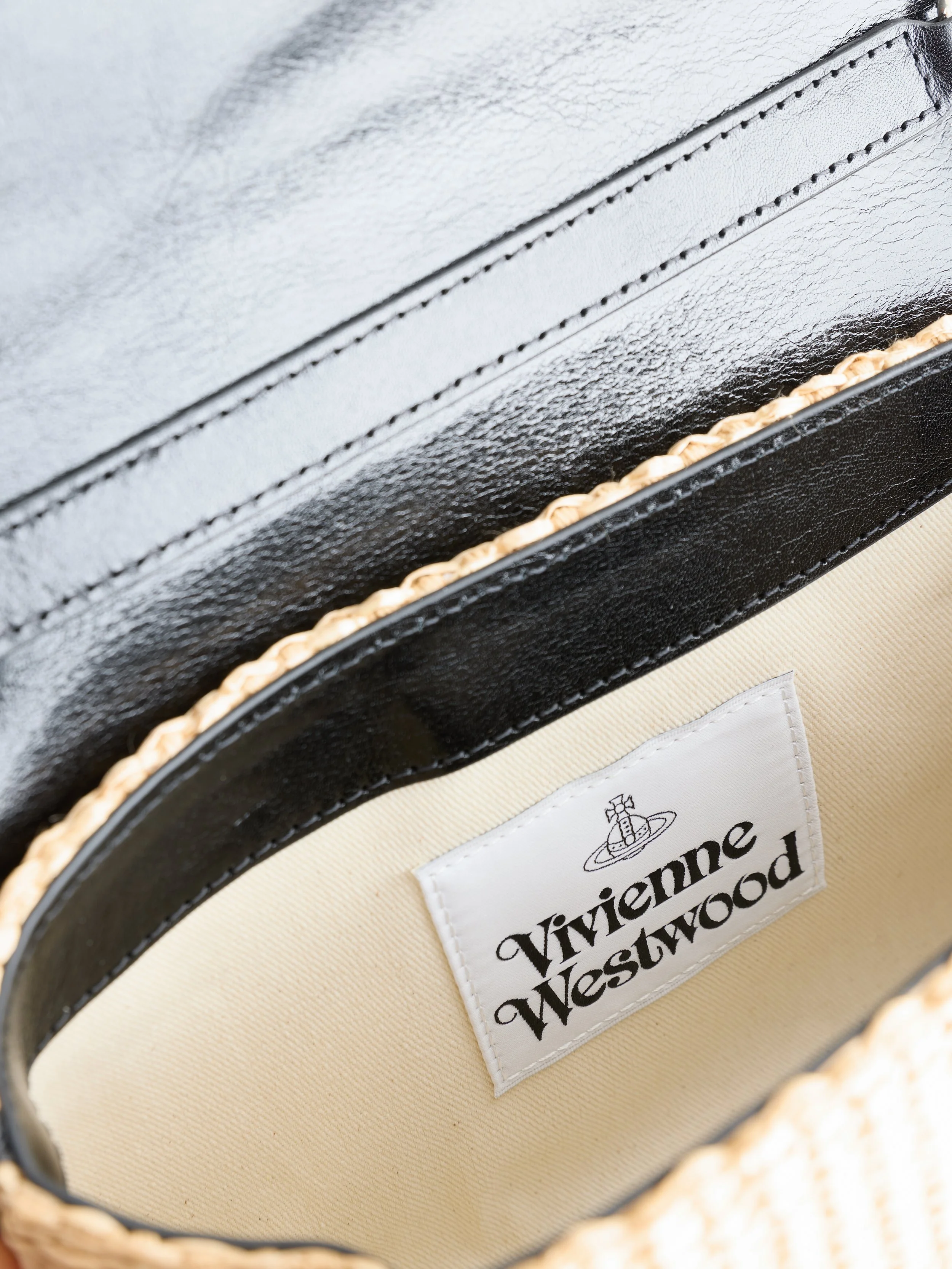 Close-up view of the interior of a beige and black bag with a white label that reads 'Vivienne Westwood' along with the brand's logo.