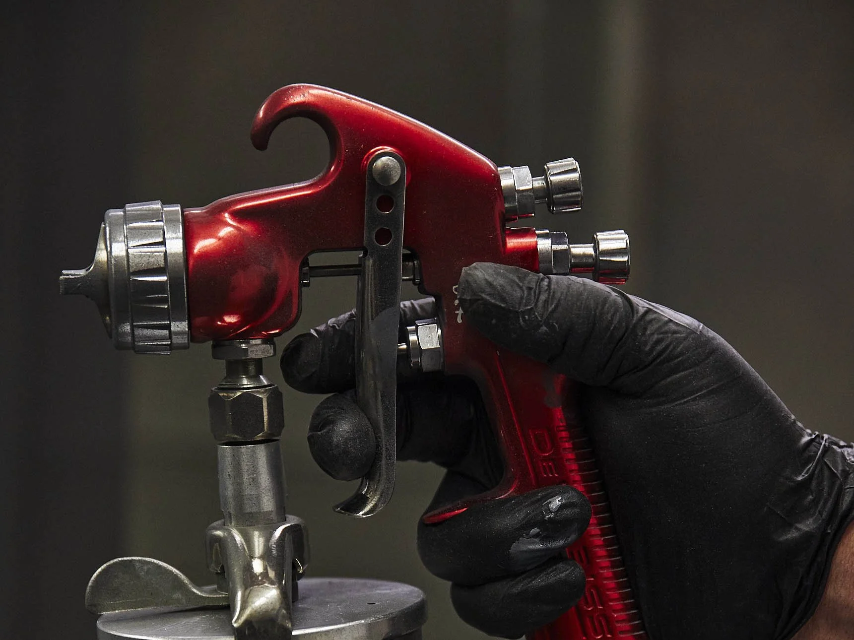A person wearing black gloves operating a red spray gun or paint gun, focusing on the tool and hand.
