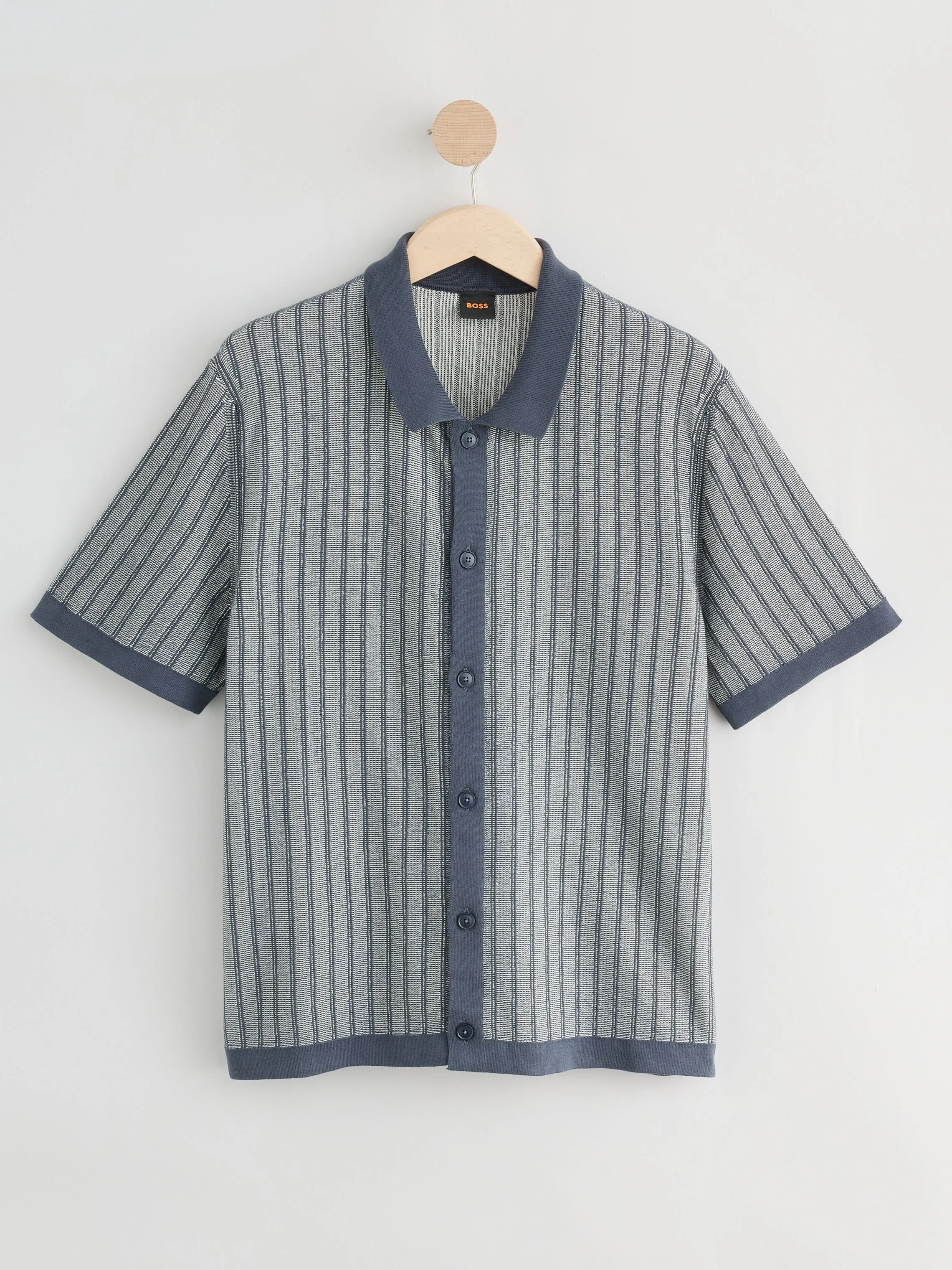 A plaid short-sleeve button-up shirt hanging on a wooden hanger against a plain white background.