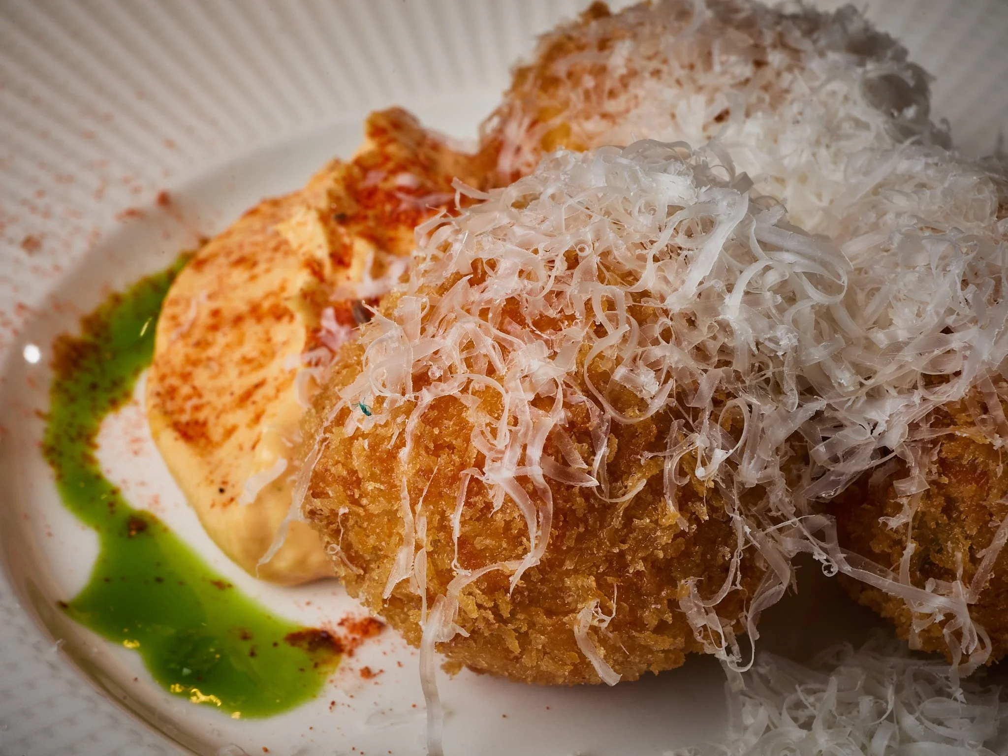 Fried food with shredded cheese on top, green sauce on side, served on a white plate