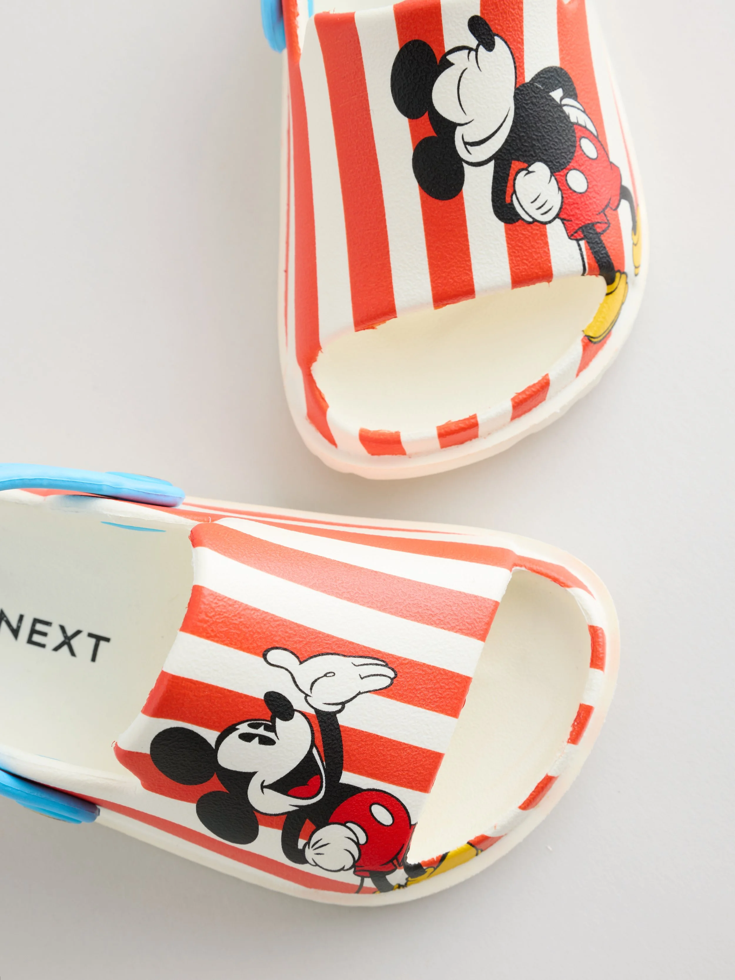 Close-up of a Mickey Mouse themed paper cup with red and white stripes, featuring Mickey smiling and holding his ear, on a white surface.