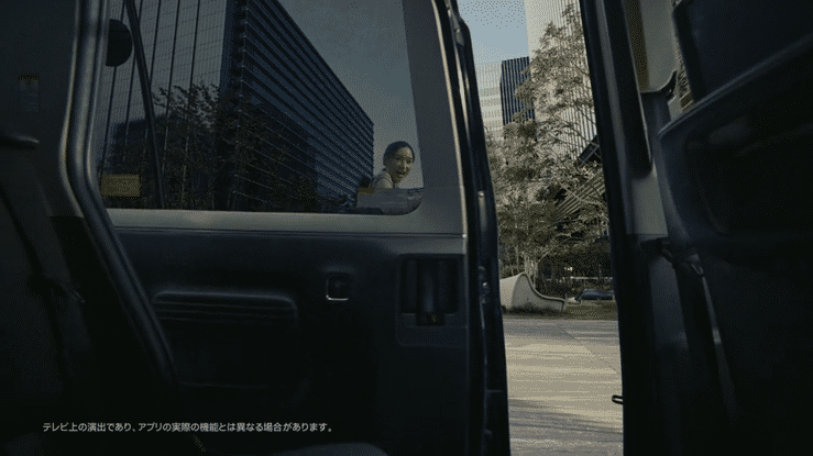 View from inside a vehicle looking out the open door at a woman in a car and modern buildings in the background during daylight.