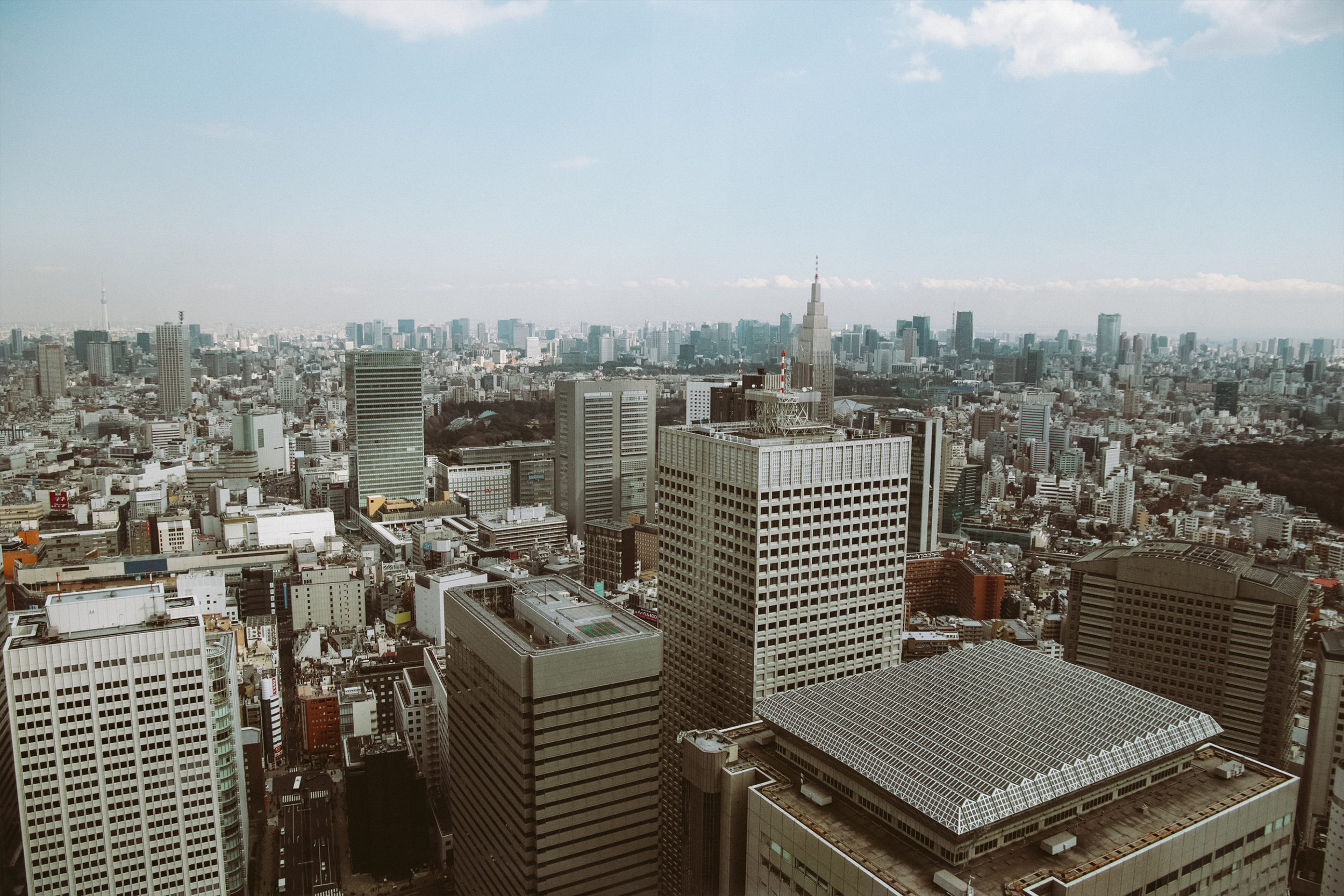 A panoramic view of a dense city skyline with tall skyscrapers and buildings, including the iconic Tokyo Tower in the center, under a clear sky.