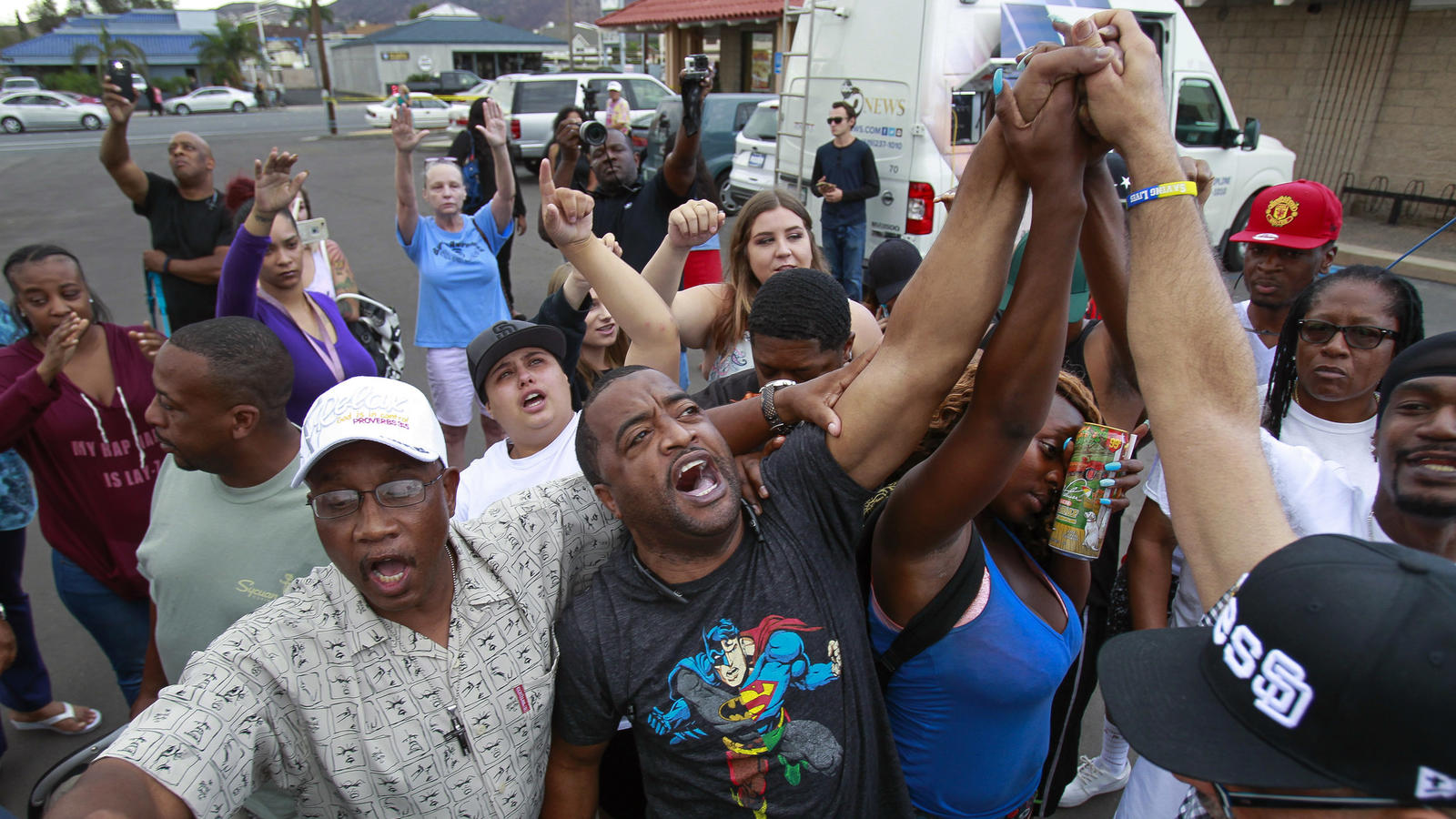 (Hayne Palmour IV / San Diego Union-Tribune. Pastor Russell Bowman, center, leads the crowd in a prayer at the scene where a black man was shot by El Cajon police earlier.
