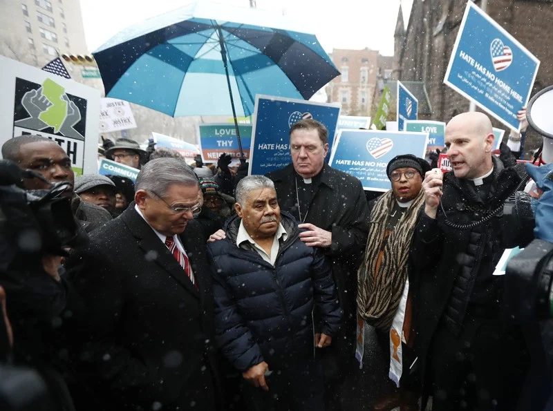 Catalino Guerrero, al centro, bajo el paraguas, es acompañado por el senador Bob Menendez, izquierda, y el cardenal Joseph Tobin, arzobispo de Newark, detrás de Guerrero, durante un mitin frente al edificio de inmigración en Newark antes de acudir a una audiencia sobre su estatus migratorio, el viernes 10 de marzo de 2017, en Newark, Nueva Jersey. Guerrero, que llegó a Estados Unidos ilegalmente en 1991, enfrenta la deportación. Los organizadores afirman que es un ciudadano sobresaliente y no debería ser deportado. JULIO CORTÉZ / ASSOCIATED PRESS