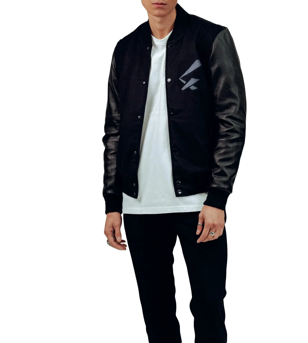 Man wearing a black varsity jacket with leather sleeves, white shirt, black pants, and rings on fingers.