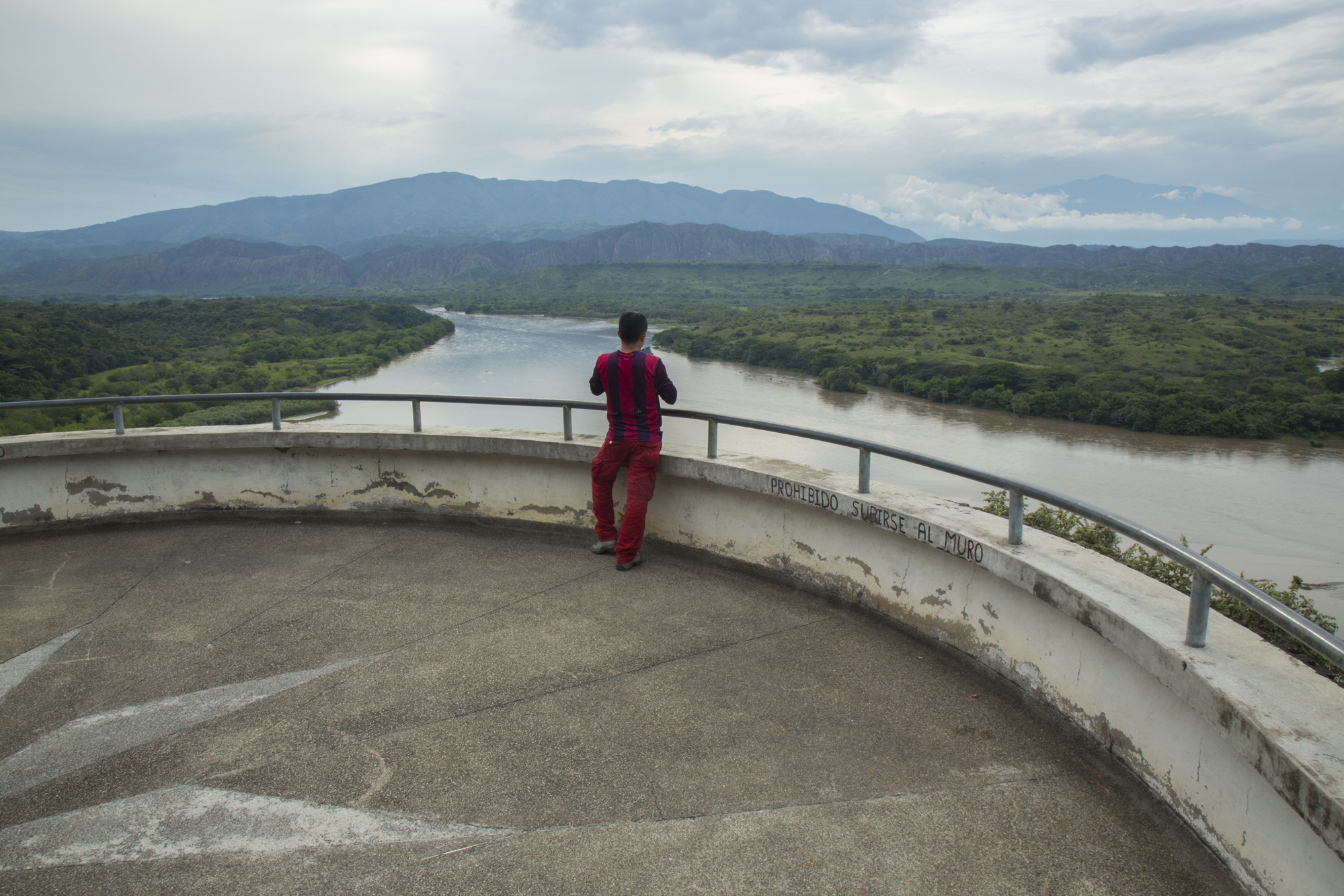  A young man observes the Magdalena River a few kilometers after the Quimbo dam from a restaurant lookout. Writing on the wall says "Forbidden to climb the wall." Local fishermen say that according to the construction of the dam, the river no longer 