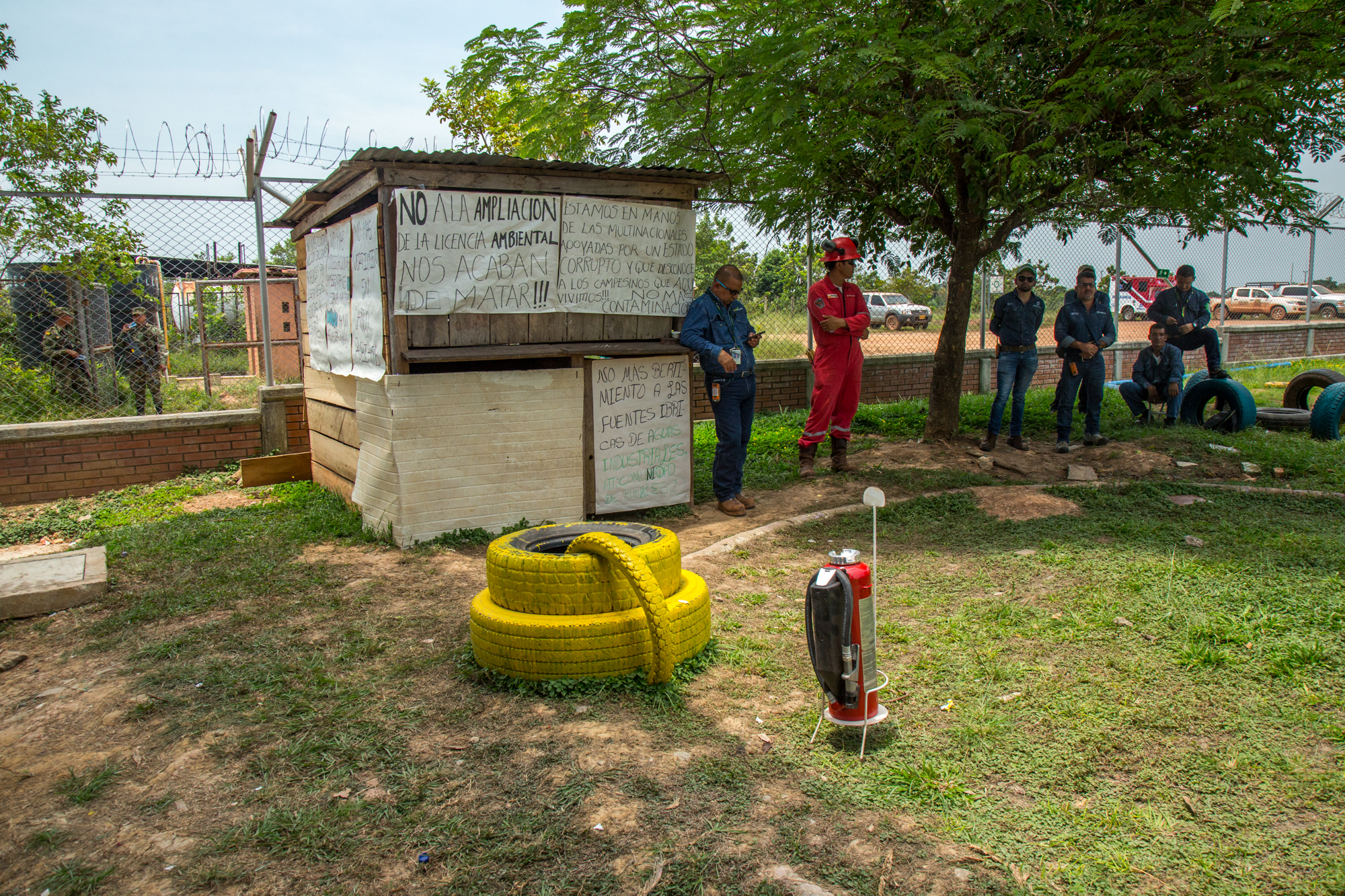  Security forces and workers stand by idly during a meeting held between Ecopetrol oil company and the local community in Rubiales, Meta. Signs posted by the community members read, "No more contamination! No amplification of the environmental licens