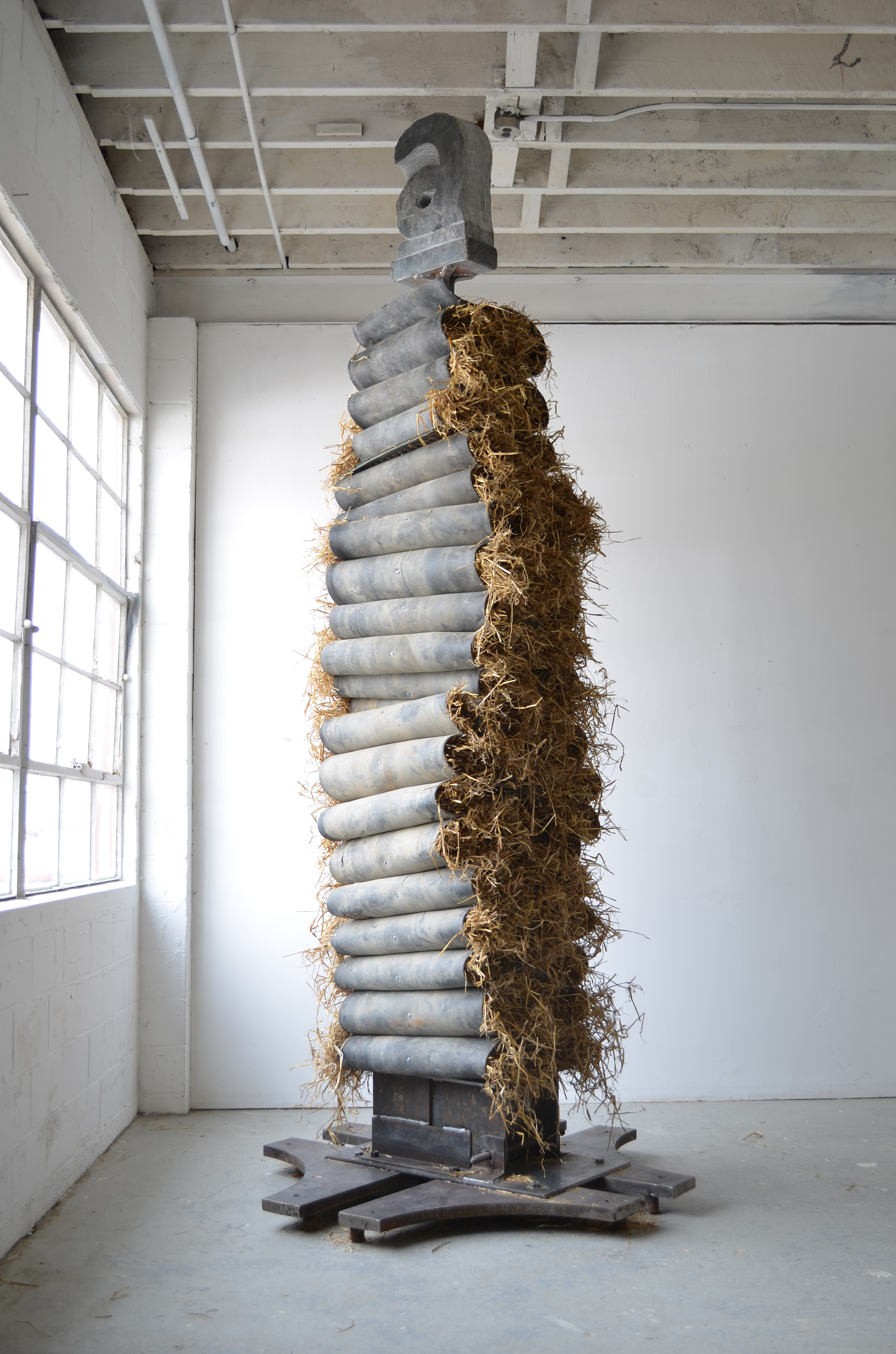 "aDay". 13' high, more than 65' of conveyor belt pierced then threaded onto steel pole, later stuffed with straw. At top is carved slate letter "a," containing red glass in the negative space of the "a."