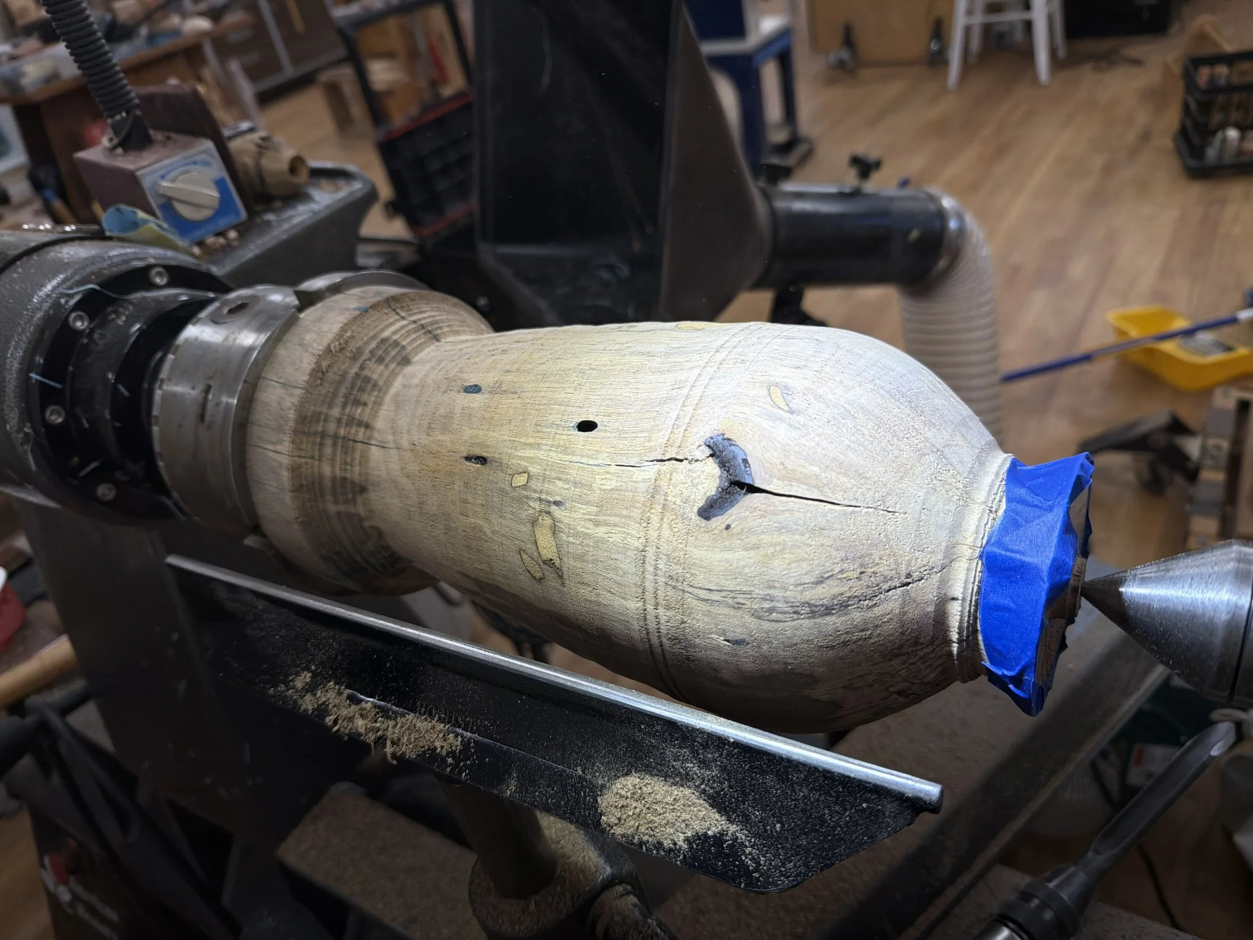 Partially shaped persimmon form on the lathe with blue painter’s tape securing a fragile section near the rim.