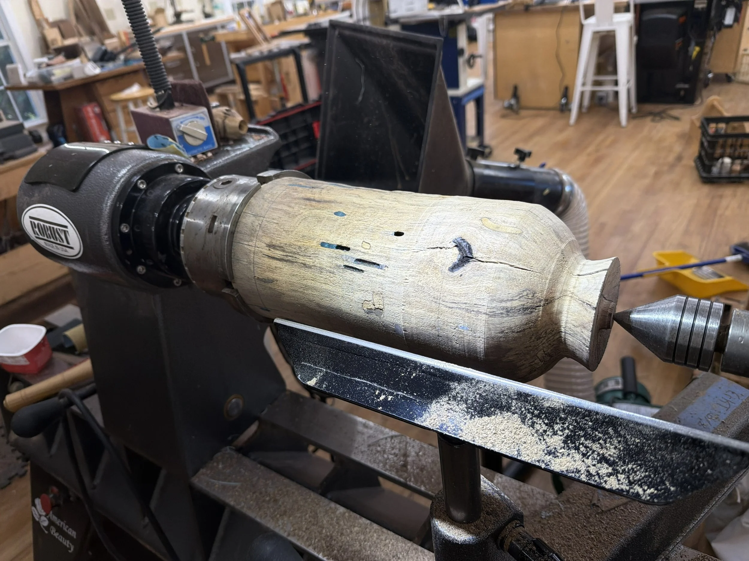 Partially shaped persimmon form on the lathe after its first resin stabilization, with filled voids visible in the pale wood