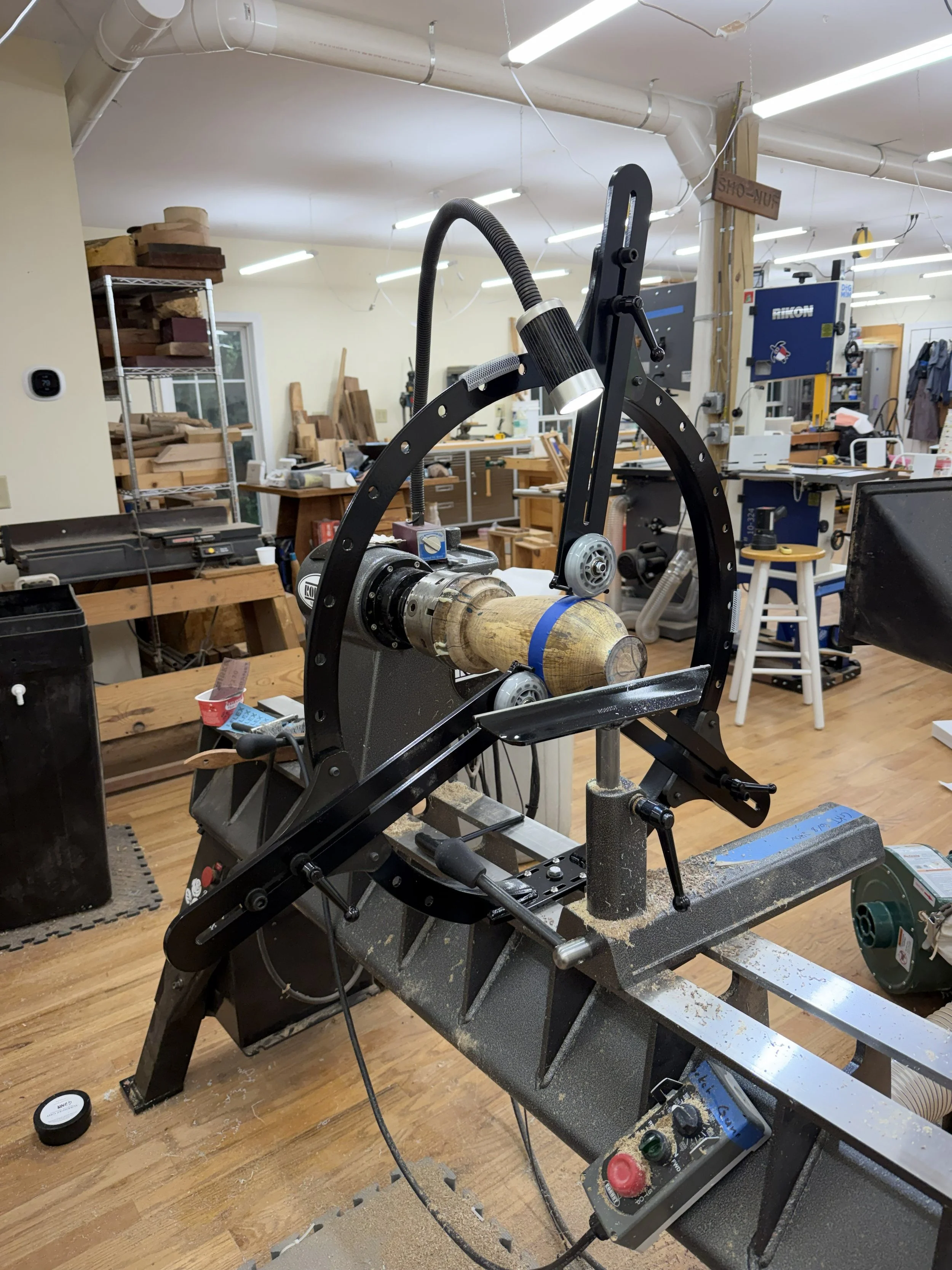 Large black steady rest surrounding the persimmon form on the lathe, with three wheels supporting the wood.