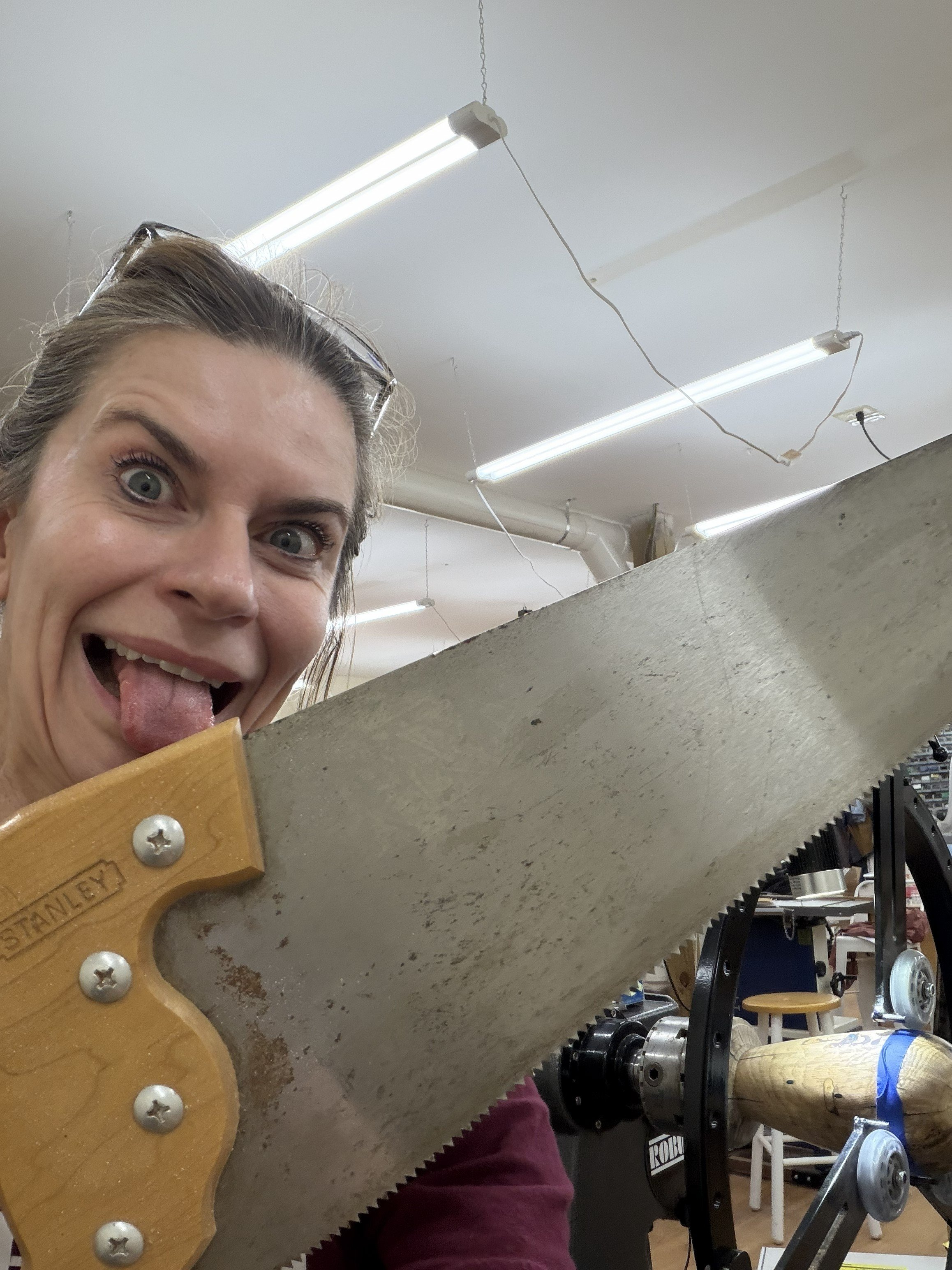 Rebekah grinning beside a large hand saw before cutting the finished persimmon hollow form free from its tenon.
