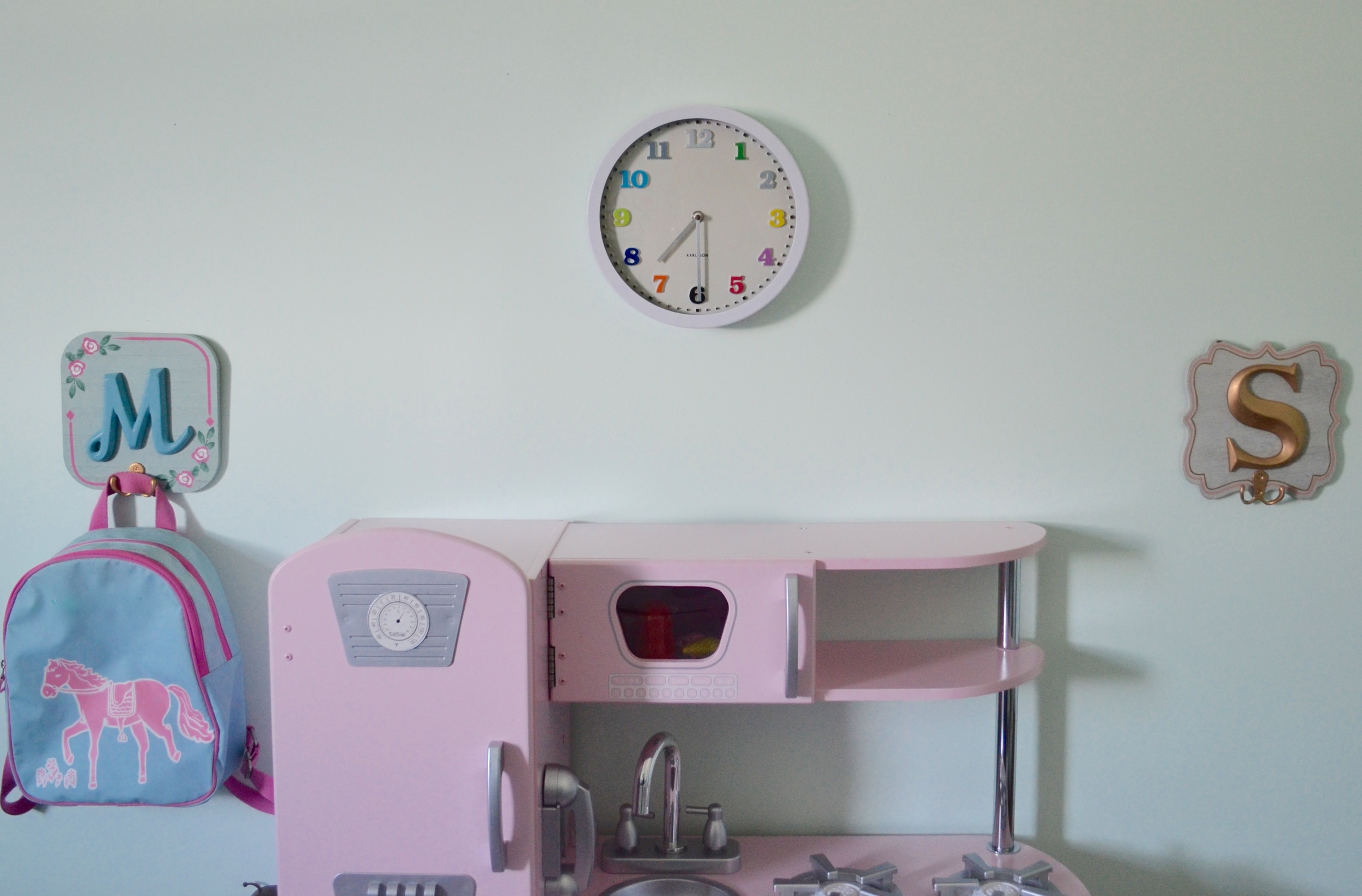 Initialed wall plaques with hooks hung at Tiny Human height are perfect for Client M to hang up her backpack after a tough day at the park. She can cook herself up something tasty in her fabulous pink play kitchen, while keeping an eye on the time.