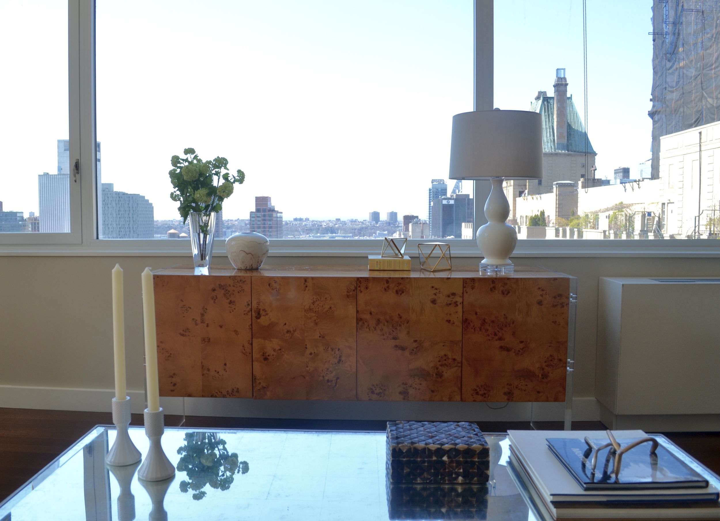 A burled-wood credenza by the window adds interest and provides a good amount of storage. It also provides another surface area and frames the beautiful view nicely with minimal/sleek accessories!
