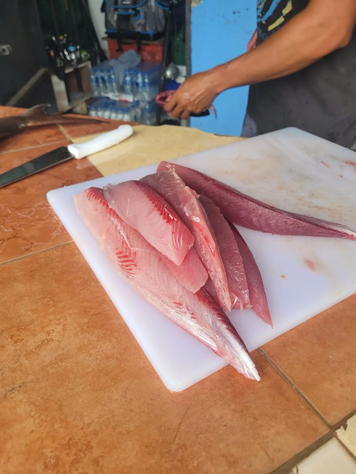 Fresh sliced fish fillets on a white cutting board in a market or kitchen setting.