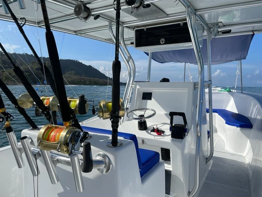 View of a boat's steering console with fishing rods mounted, overlooking a body of water with land and mountains in the background.
