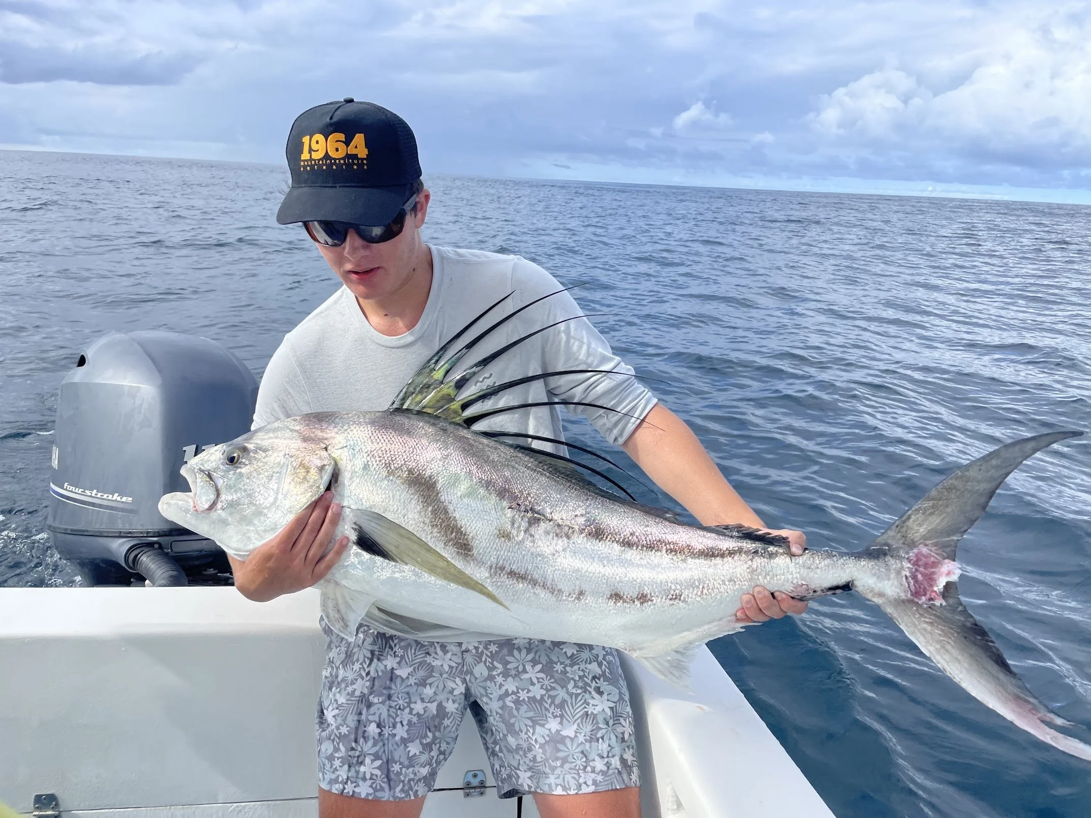 Person holding a large fish on a boat with ocean and cloudy sky in background