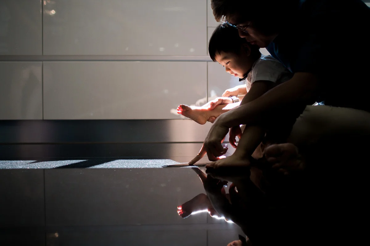A father and his toddler son play in reflective light at home in Kuala Lumpur.