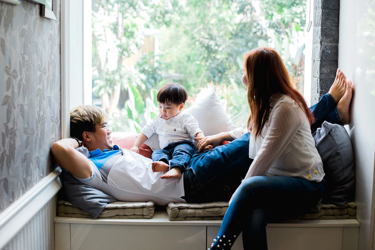 A lifestyle family photoshoot featuring a young family and their toddler son lounging in a window seat, at home in Kuala Lumpur.