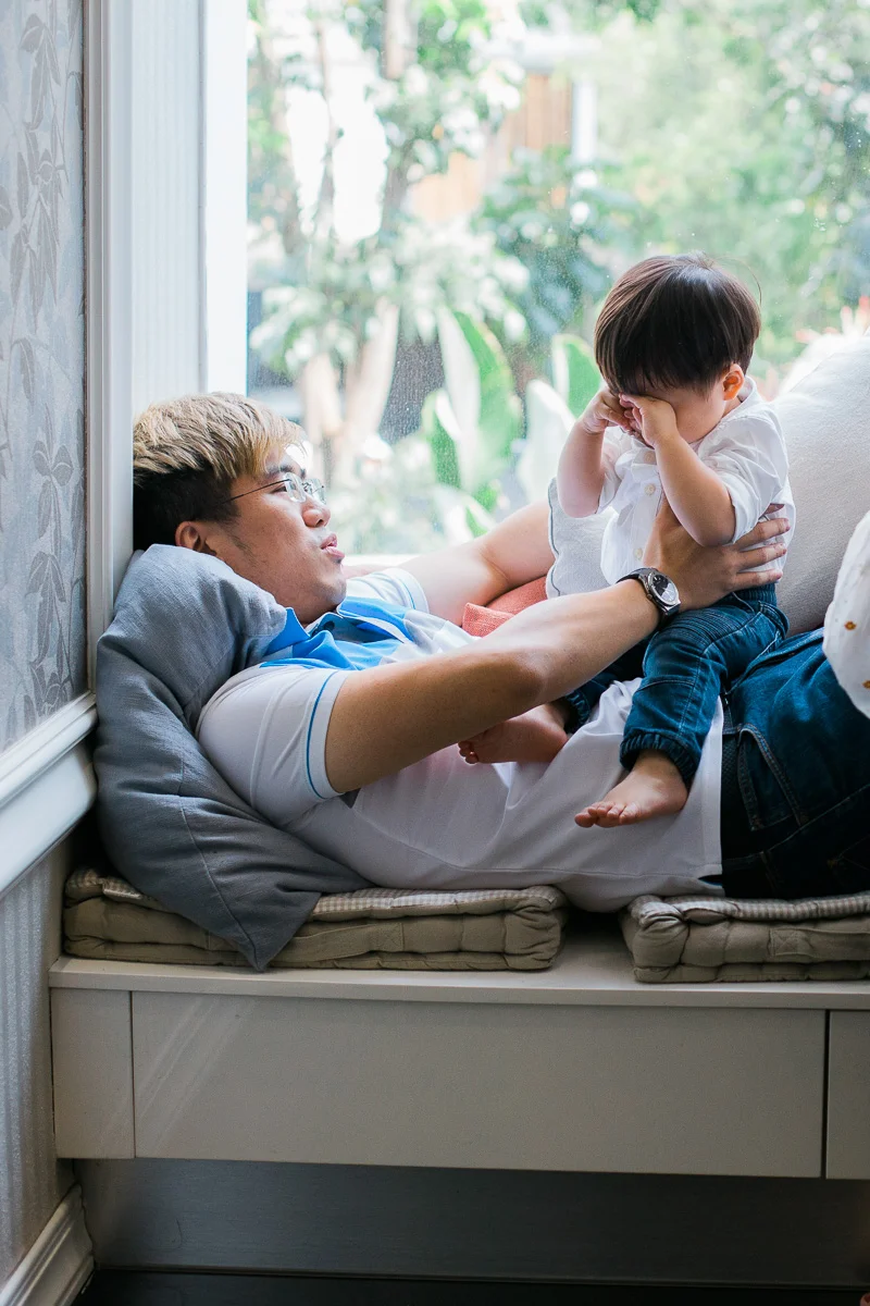 A tired little boy sits on his father’s belly and rubs his eyes during a family photoshoot in Kuala Lumpur.