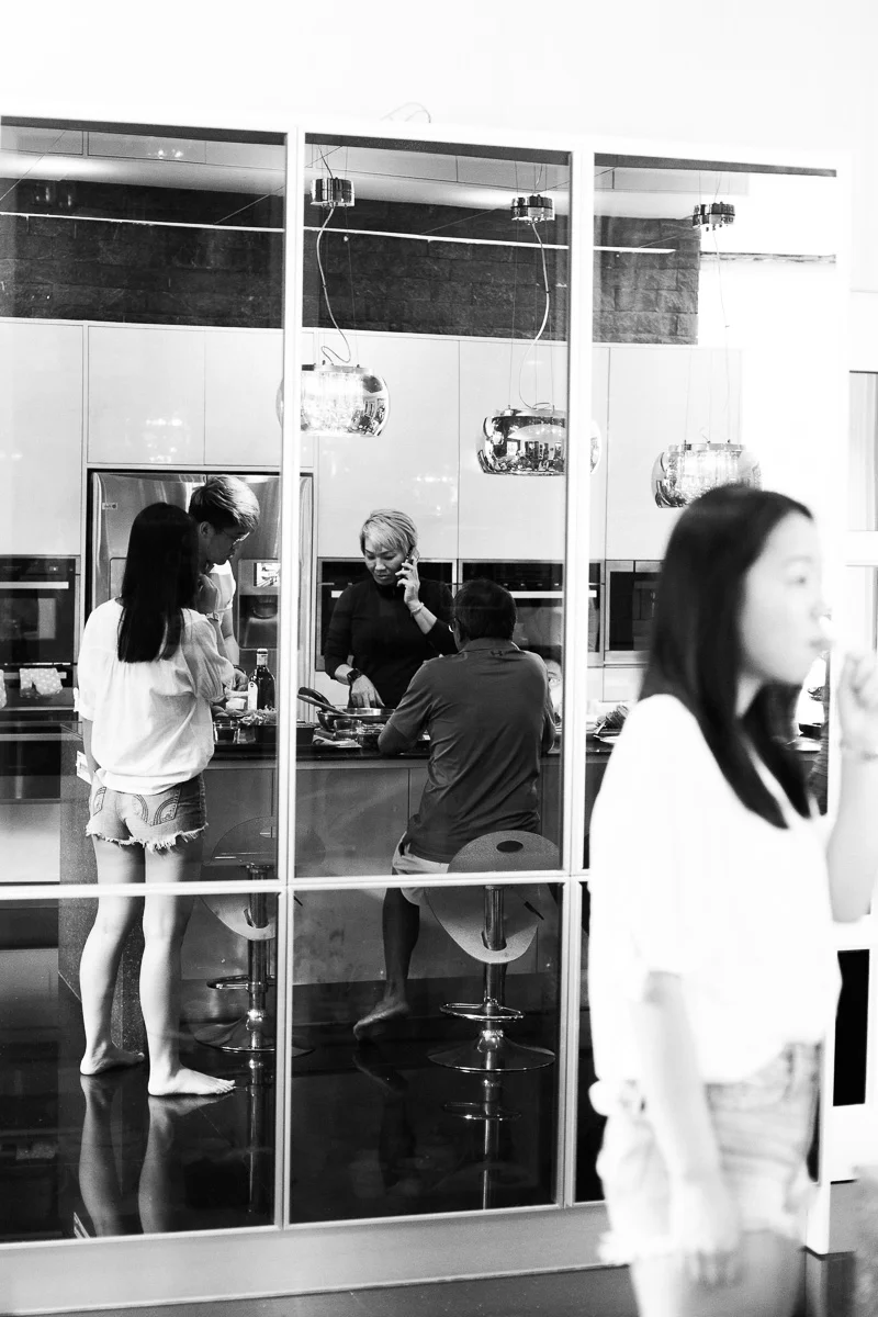A documentary style images in black and white showing a large family gathering around a kitchen island at home in Kuala Lumpur.