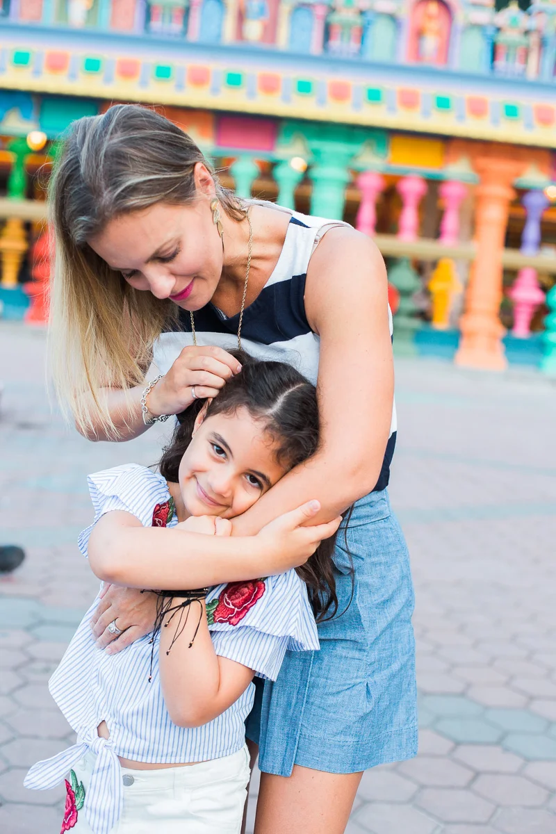 A mother embraces her daughter in front of the colourful facade of a Hindu Temple by Kuala Lumpur photographer Erica Knecht.