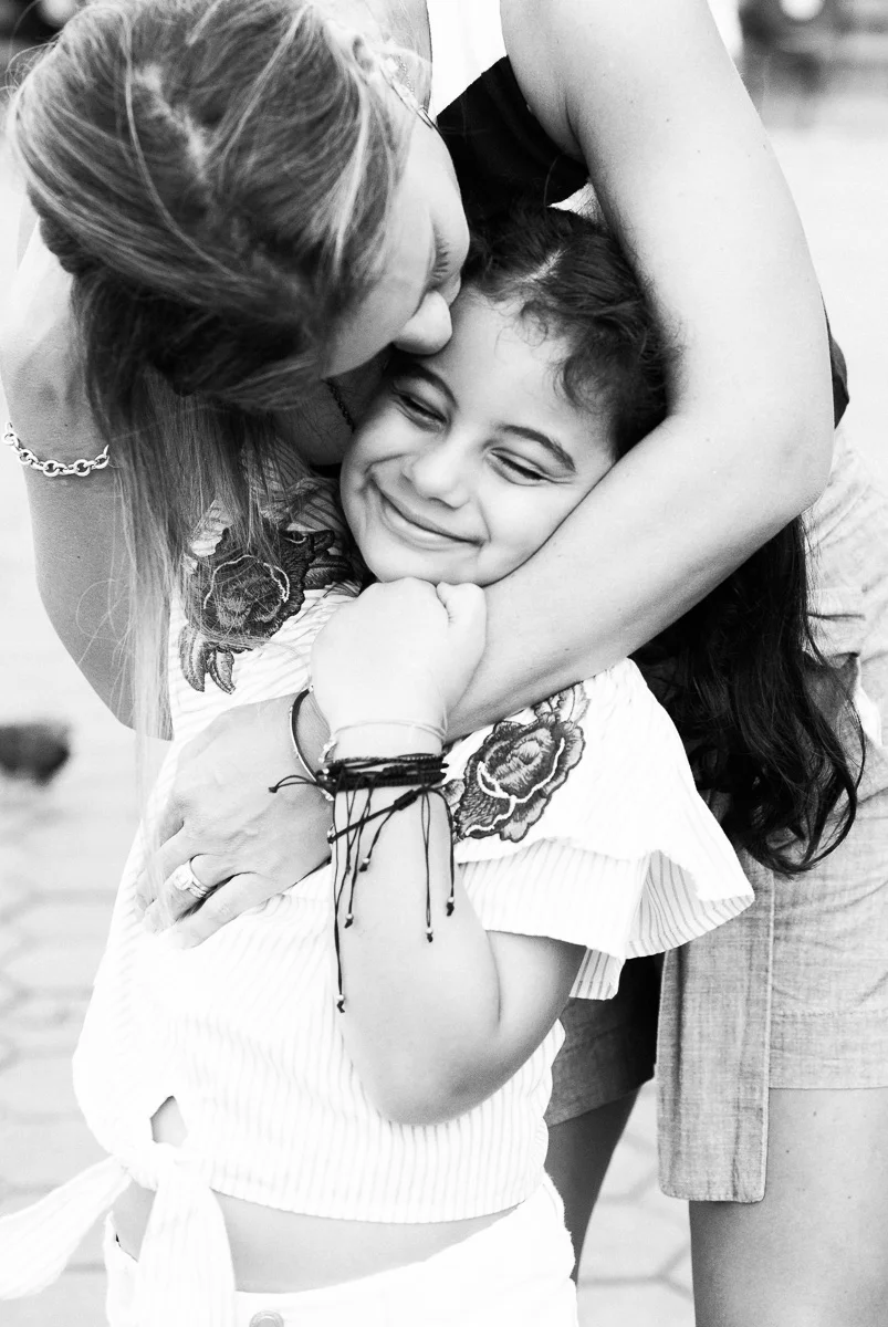 A black and white image of a mother embracing her smiling daughter in Kuala Lumpur by family photographer Erica Knecht.