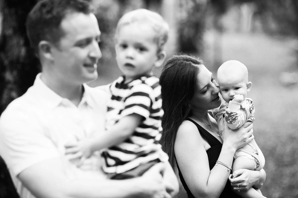 A black and white image of a young family cuddling together in KLCC Park by Asia family Photographer Erica Knecht.