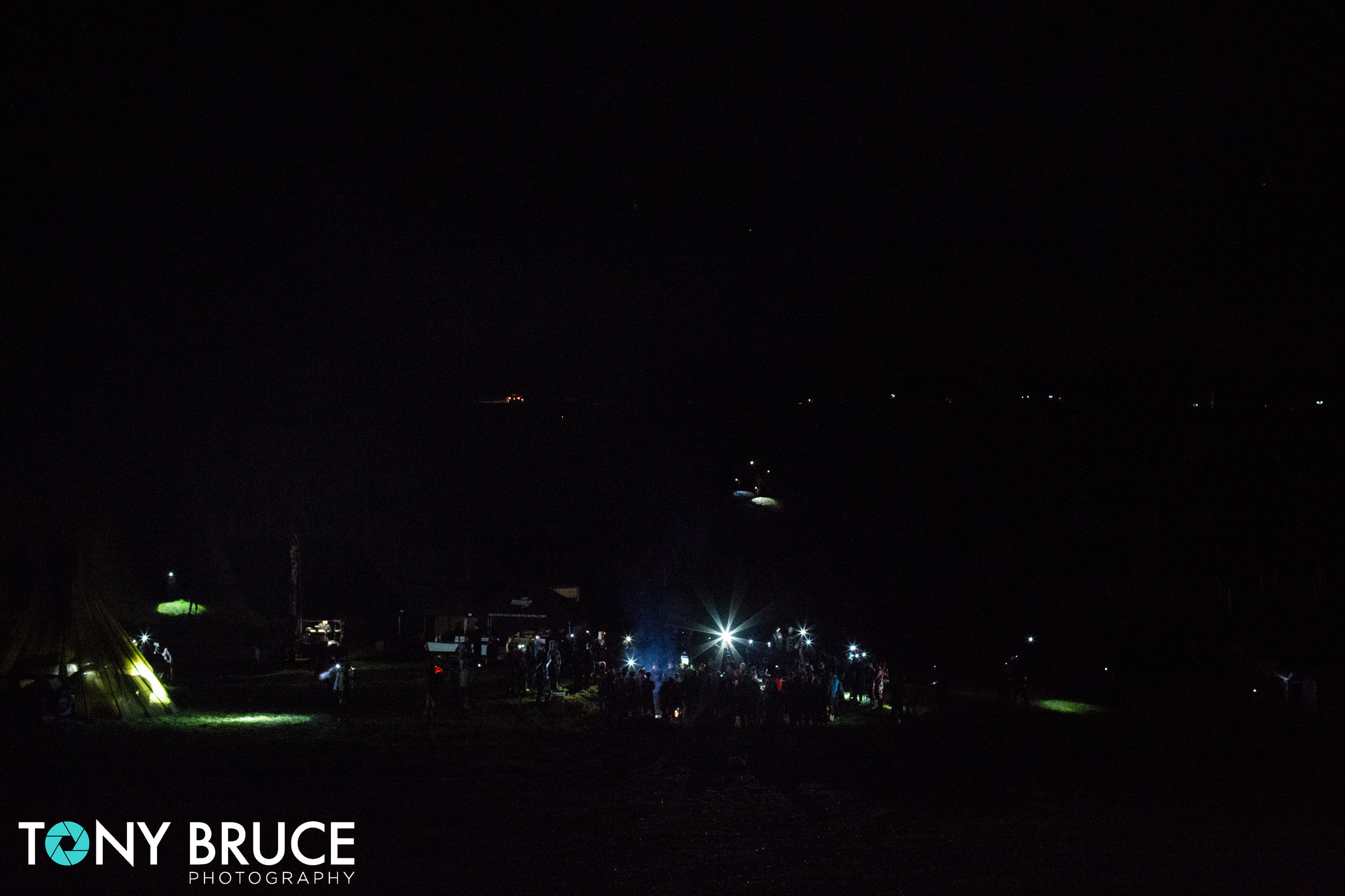In the foreground competitors gather round the camp fire for a motivational speech from Coach Pain. At the top of the image late comers' head torches can be seen as they wind their way down the valley.