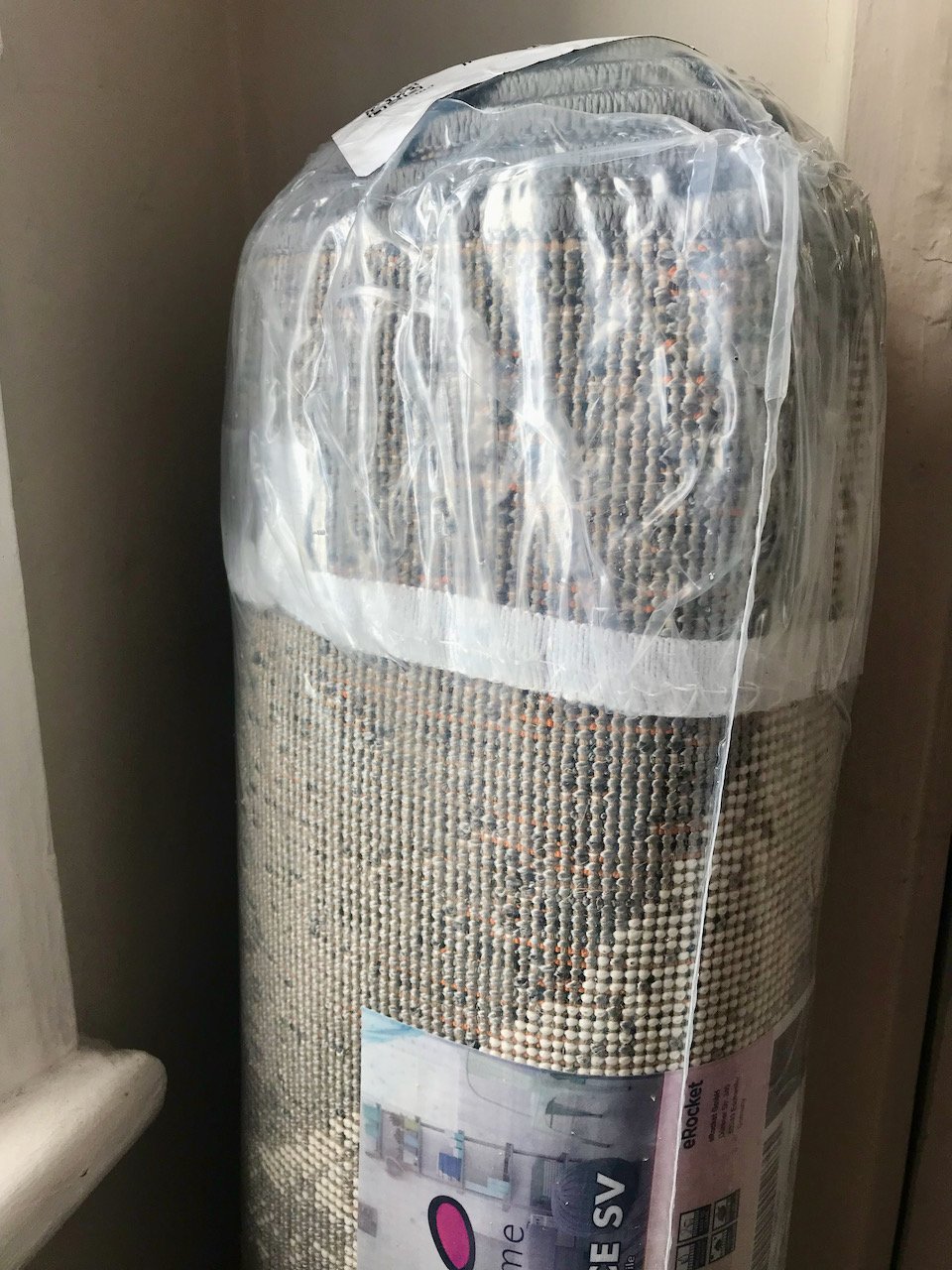 A rug that's wrapped up and in its packaging standing on its end