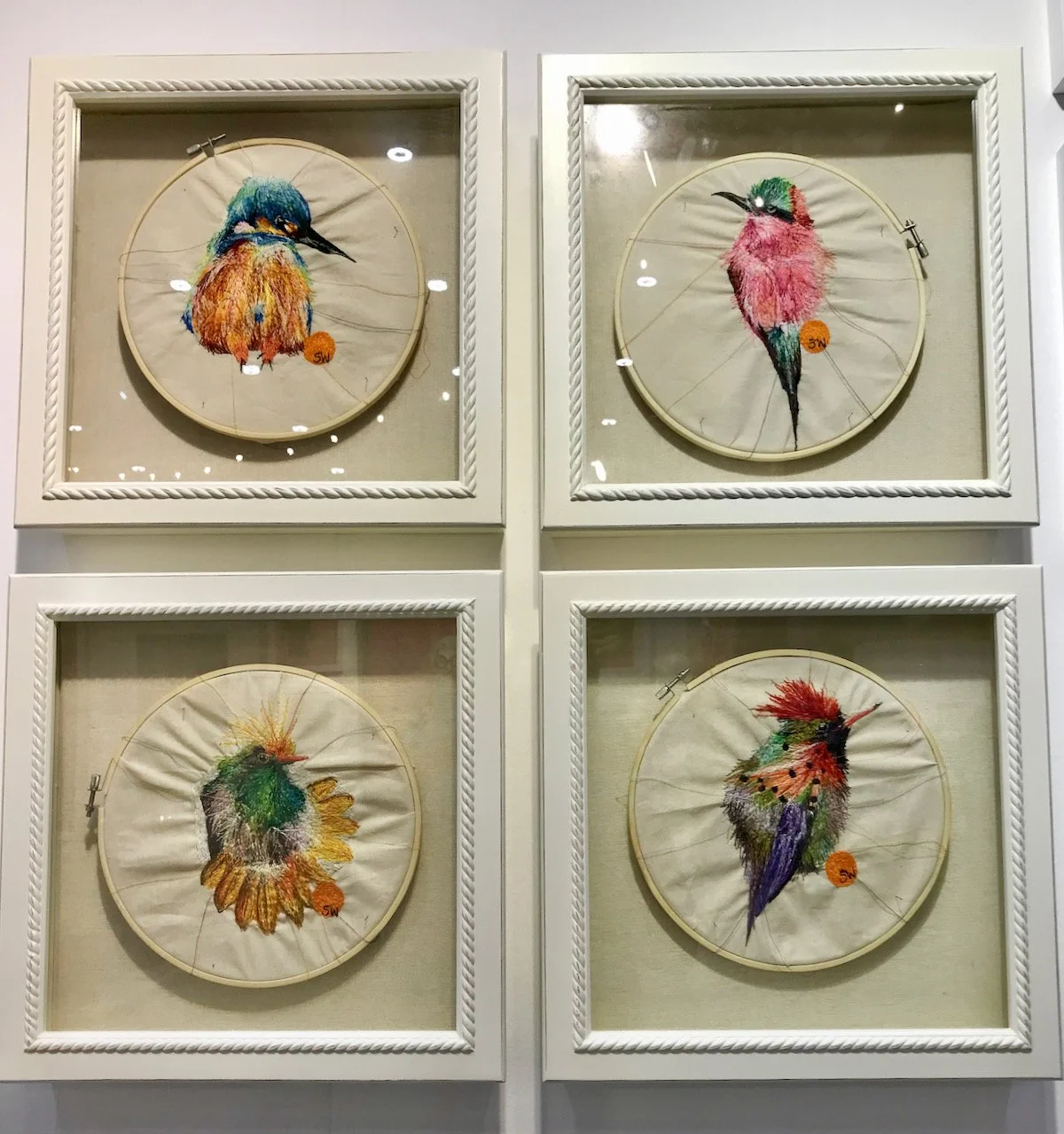 A set of four square framed embroidered birds heads which remain in their embroidery hoop